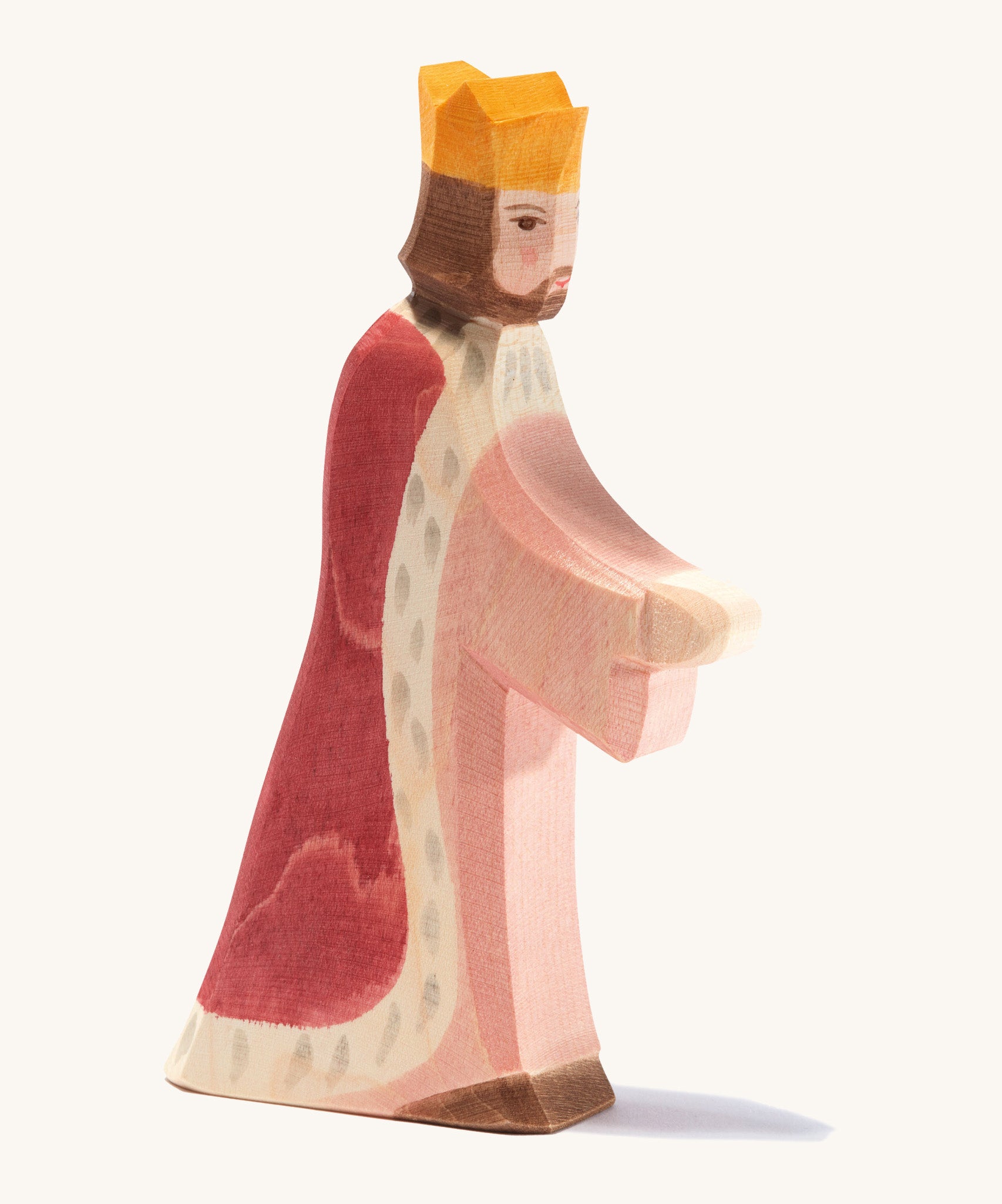 A Ostheimer wooden king figure wearing a pink gown and red cloak with a gold crown on his head on a cream background.