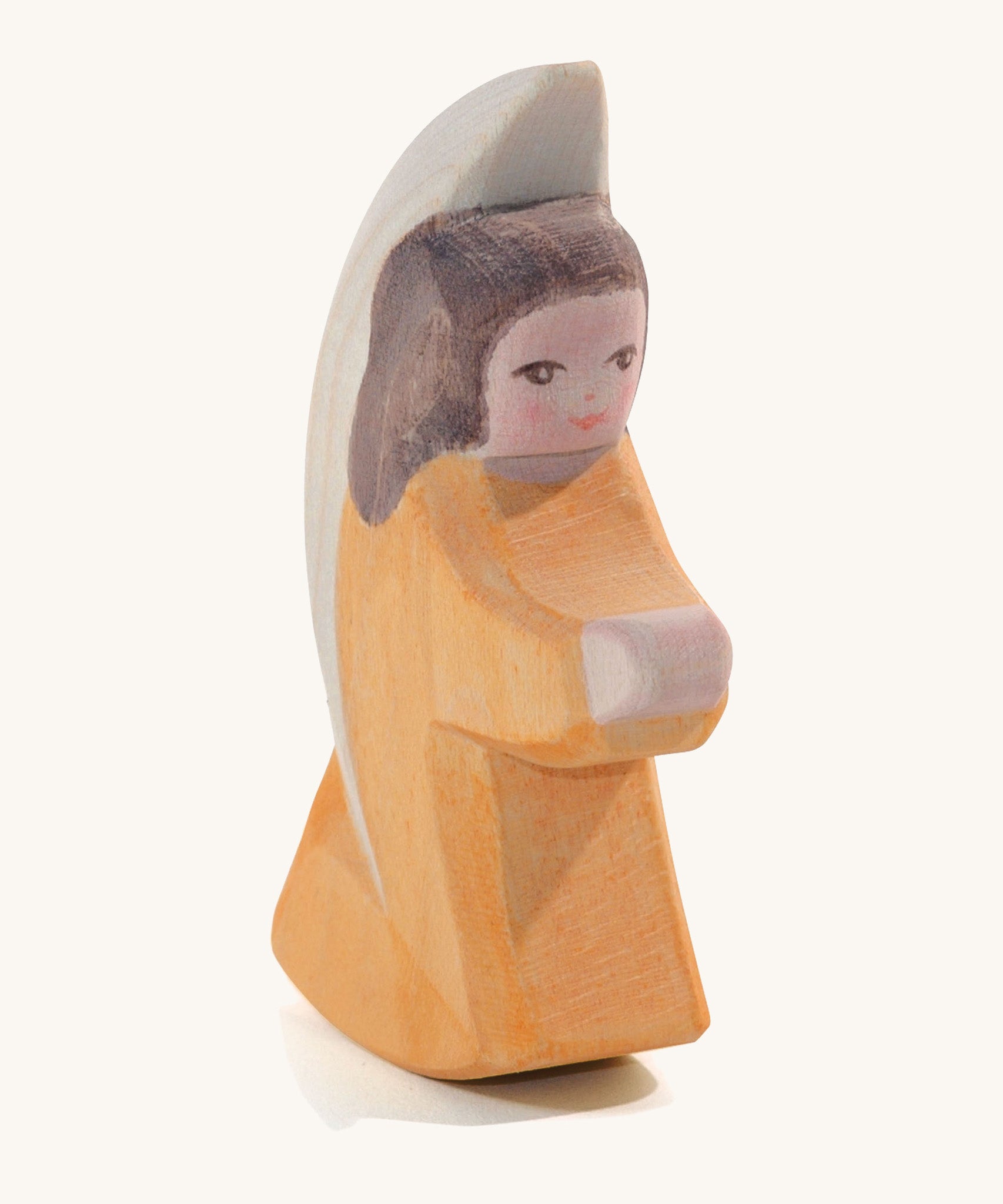 A wooden orange Ostheimer little angel figure on a cream background.