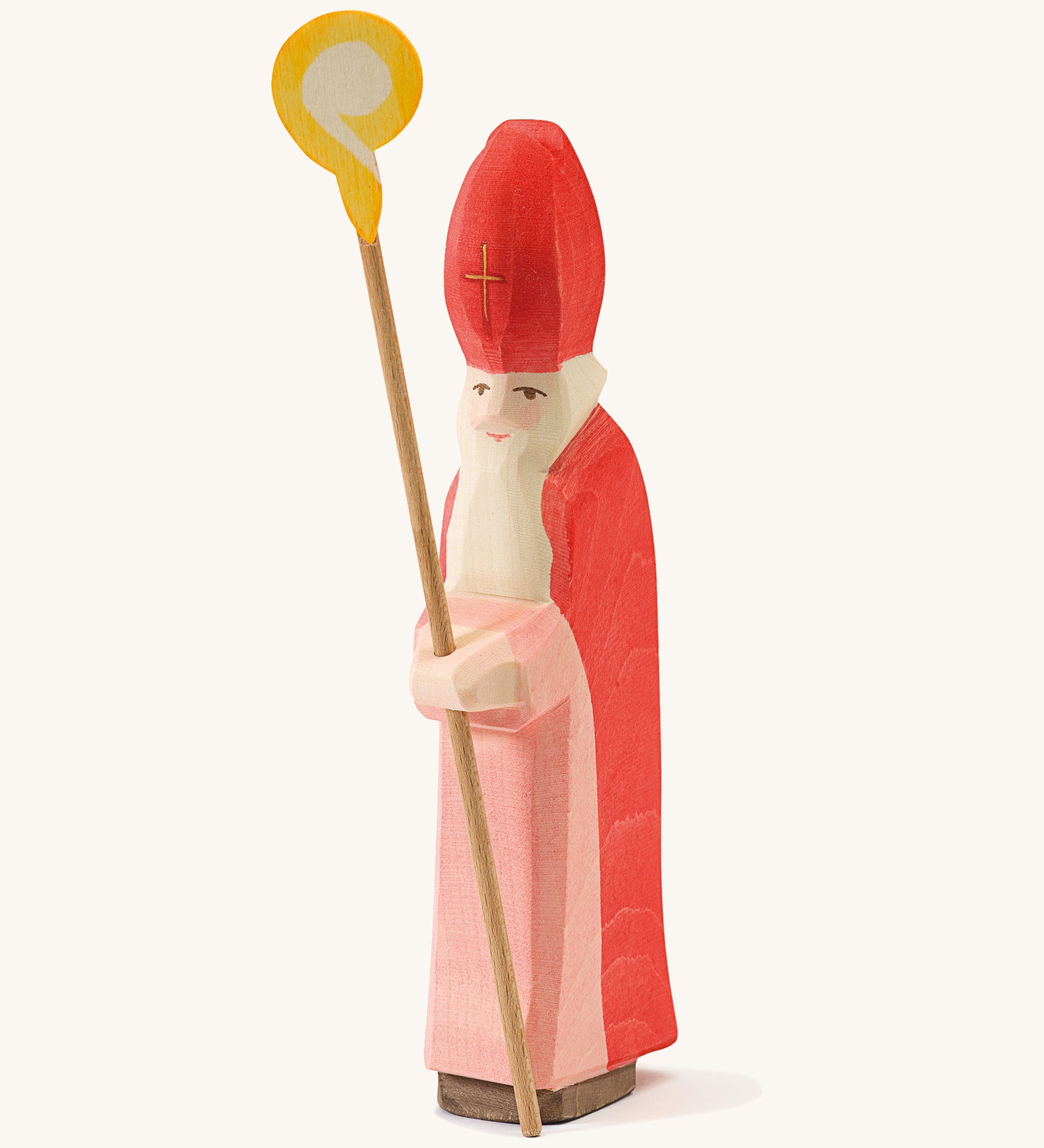  A wooden Ostheimer St Nicholas figure wearing a red gown and matching red hat holding a wooden staff on a cream background.