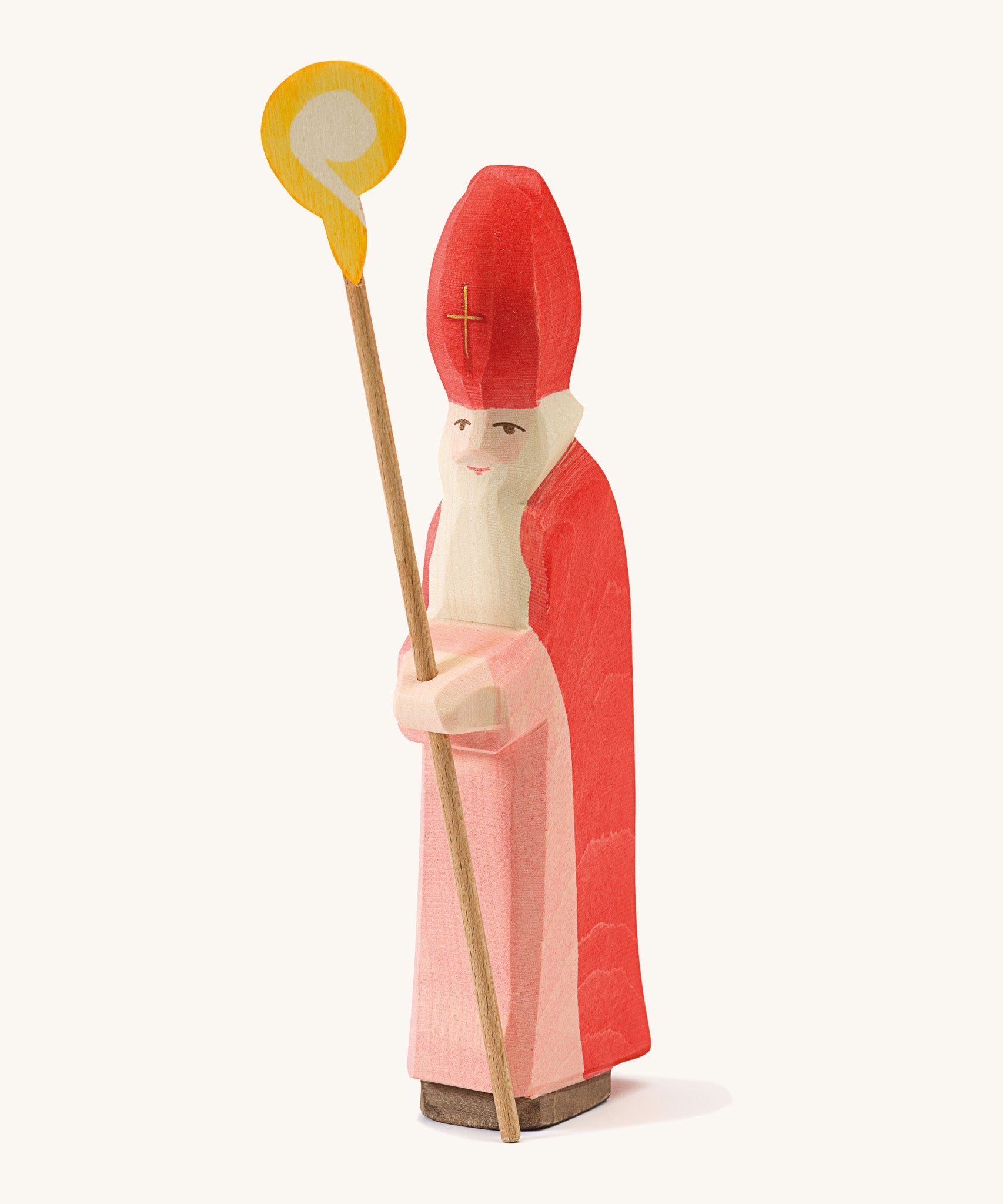  A wooden Ostheimer St Nicholas figure wearing a red gown and matching red hat holding a wooden staff on a cream background.