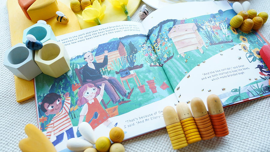 'Omar and the Bees' story book open on a table, surrounded by Babipur wooden toys