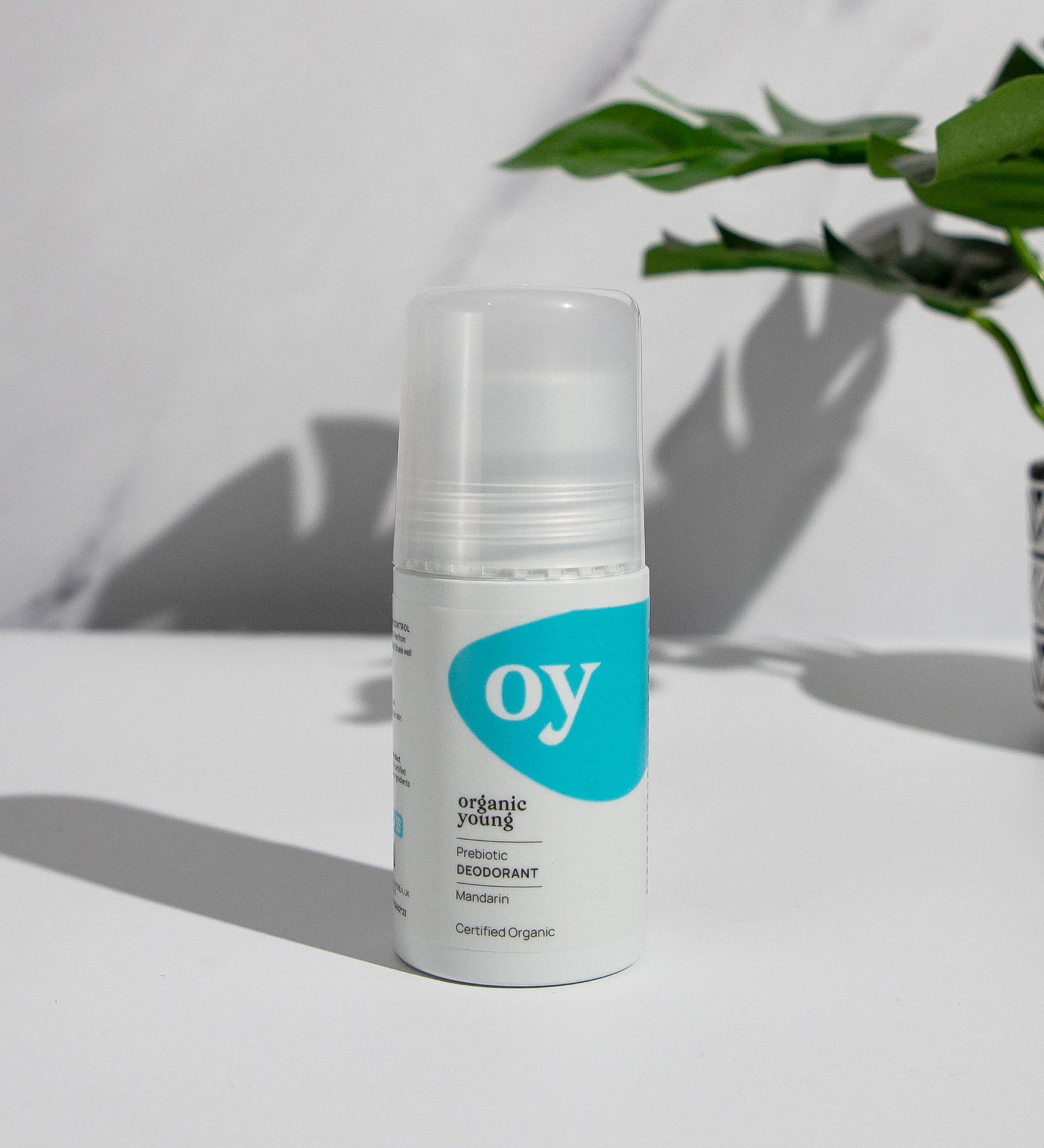 The Green People OY! Organic Teen Deodorant is stood on a white table, with a grey and white marble backgoound, and a green plant in the upper right corner