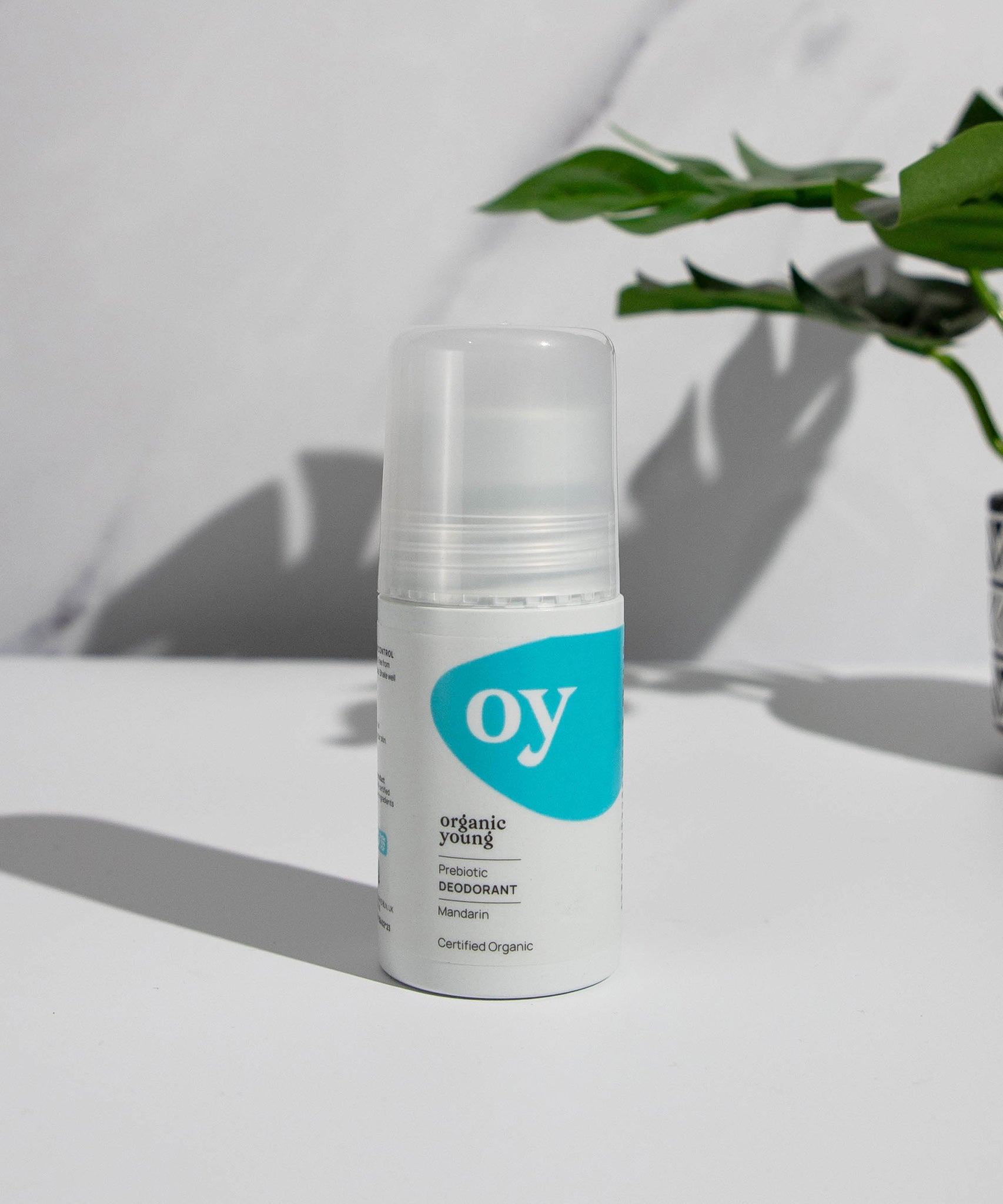 The Green People OY! Organic Teen Deodorant is stood on a white table, with a grey and white marble backgoound, and a green plant in the upper right corner