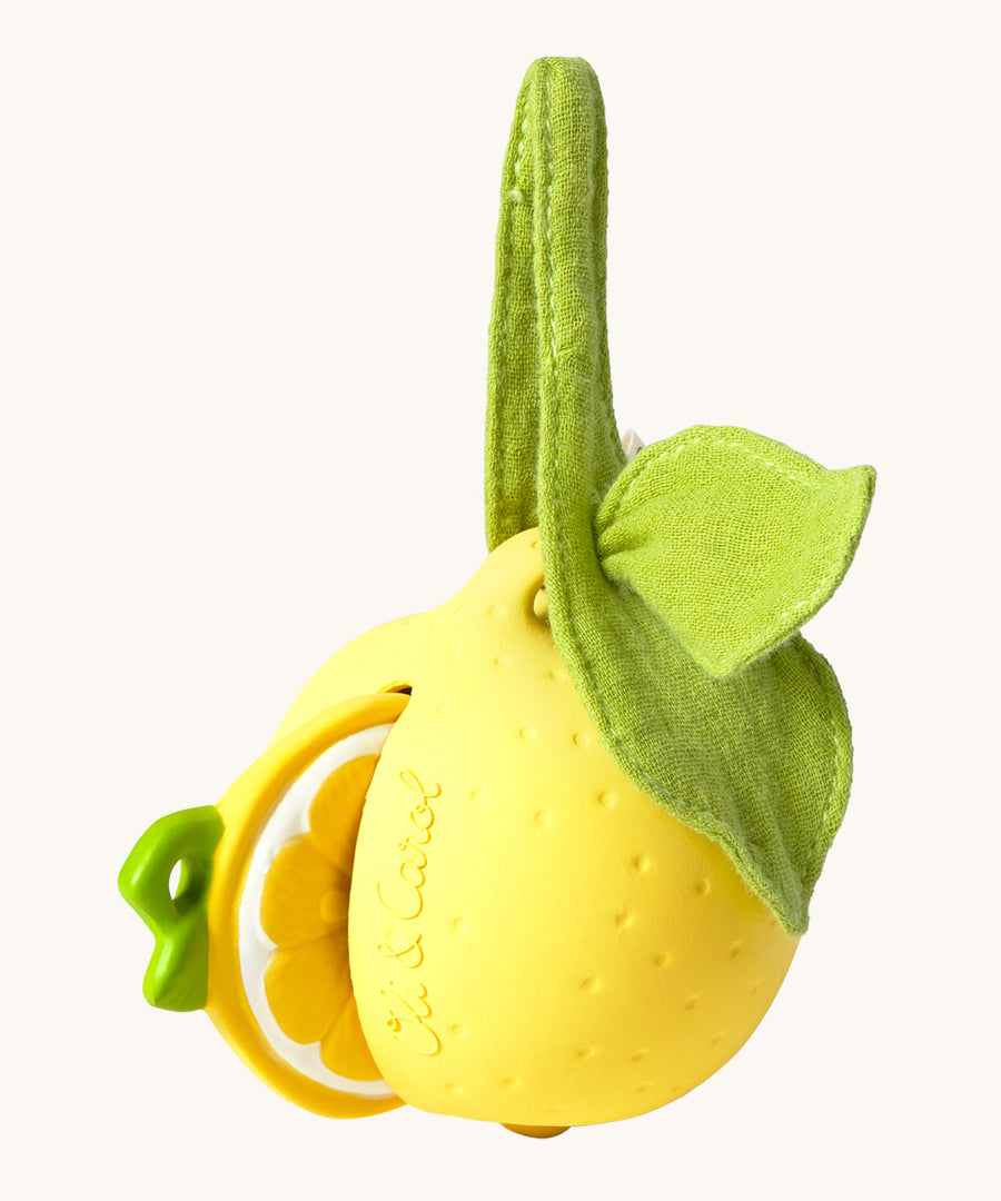 The Lou the Lemon Pacifier Holder on a cream background. The image shows an Oli & Carol lemon teething toy half way inside the holder. The lemon is textured and has a green muslin leaf attachment on the top to tie the holder to a pram handle, high chair etc.