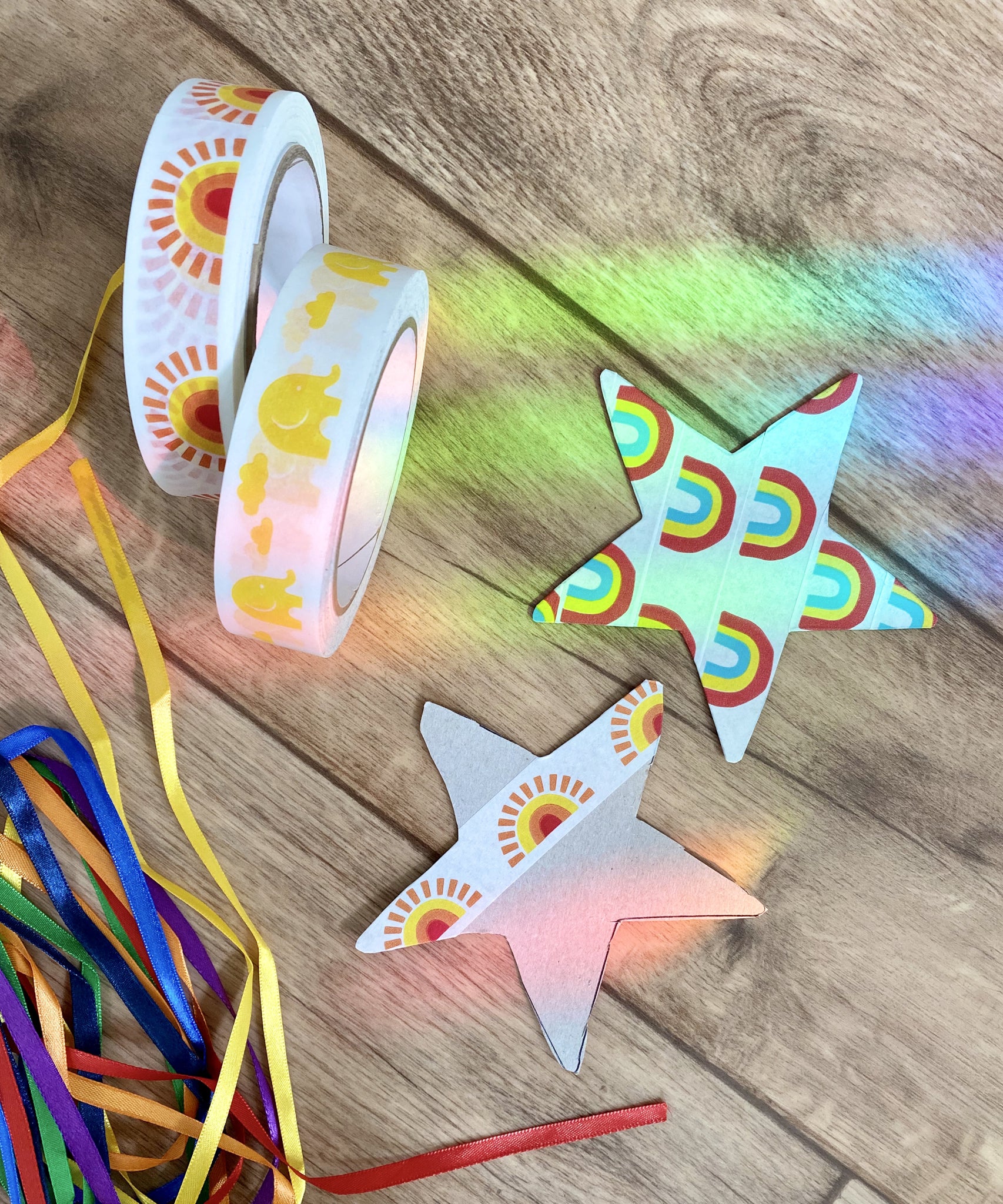 Two cardboard stars decorated with Babipur tape on the floor next to two rolls on Babipur tape.