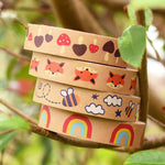 A stack of Babipur Kraft Eco Paper Tape including Mushroom, Fox, Bee and Rainbow, in an outdoor setting