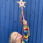 Child holding a cardboard star wand that's edged with Babipur rainbow tape. The child is stood in front of a blue shed.