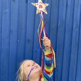 Child holding a cardboard star wand that's edged with Babipur rainbow tape. The child is stood in front of a blue shed.