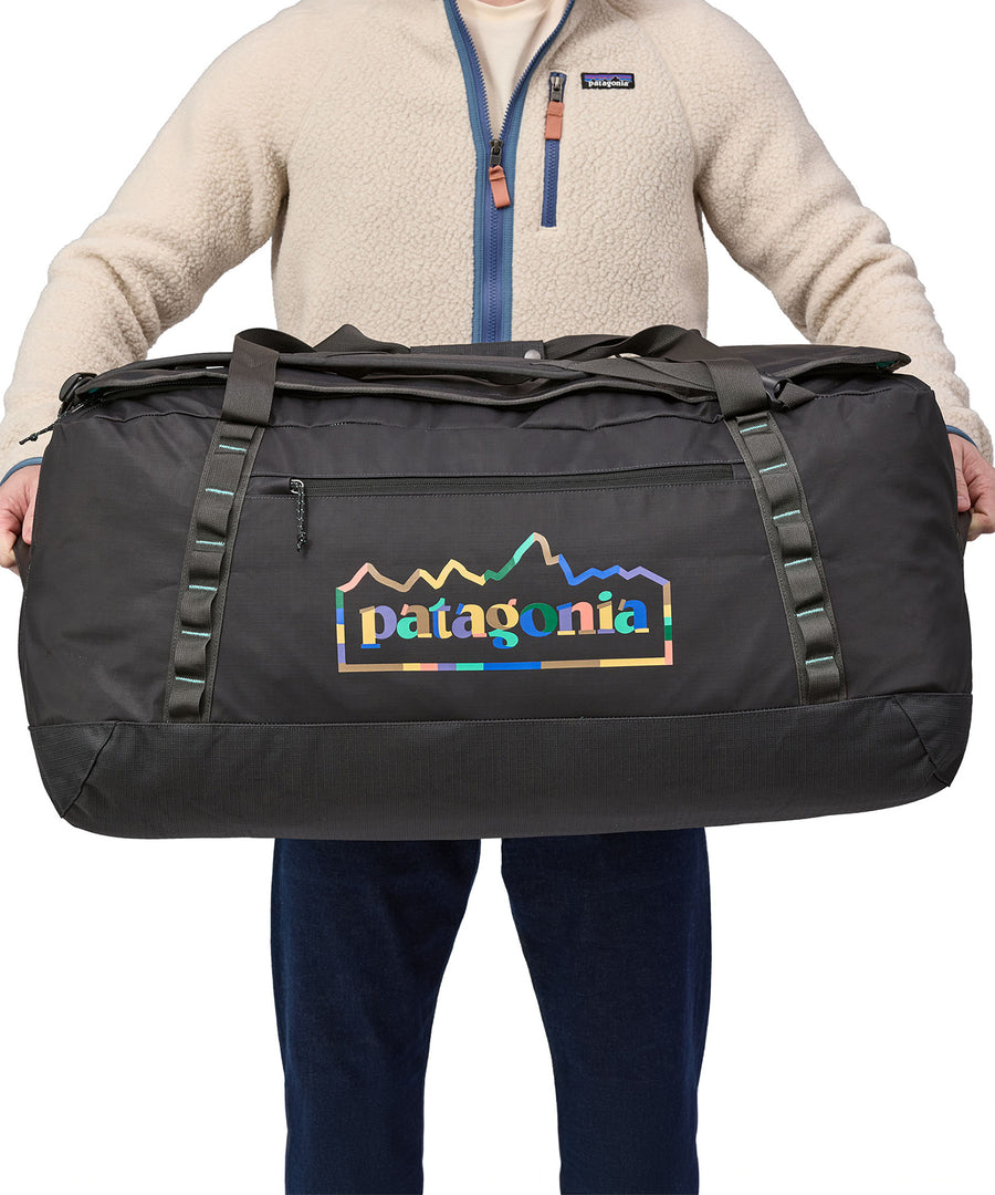 A person holding the Patagonia Black Hole Duffel 100L Ink Black in their hands, showing the size