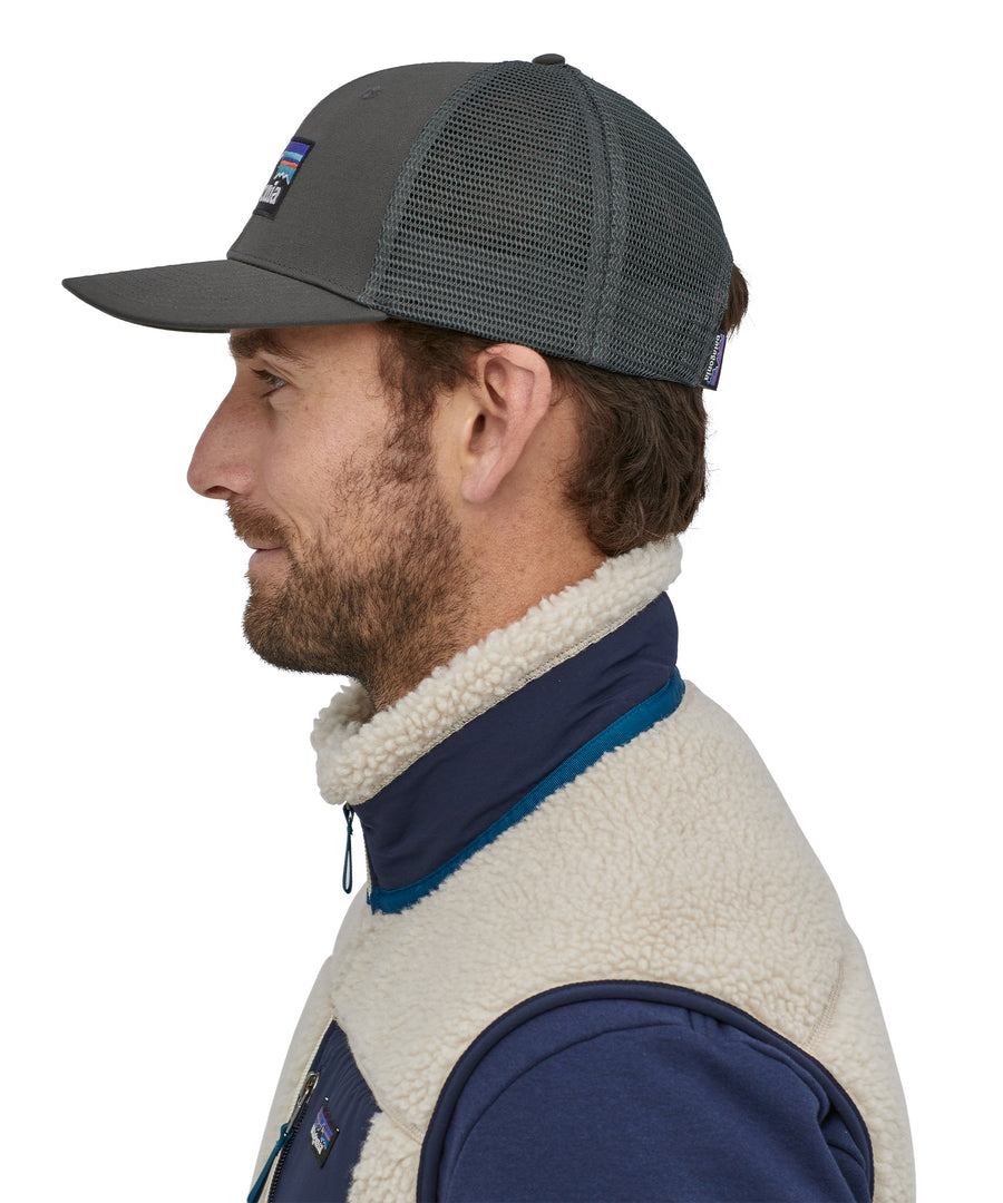 A person wearing the Patagonia P-6 Logo Trucker Hat - Forge Grey, showing it from the side to show the mesh at the back