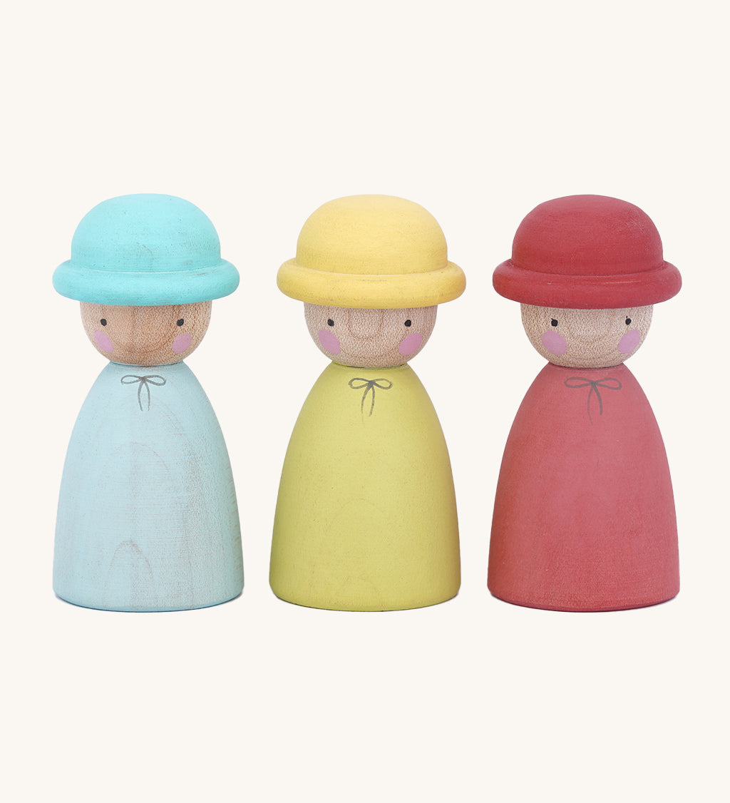 The Peepul Three Hatters are Waldorf inspired, wooden peg dolls with little bowler hats. The peg doll on the left is blue with a blue hat, the middle is yellow with a yellow hat, and the one on the right is red with a red hat. Each doll has two small, black eyes and two pink rosy cheeks. The image is on a cream background