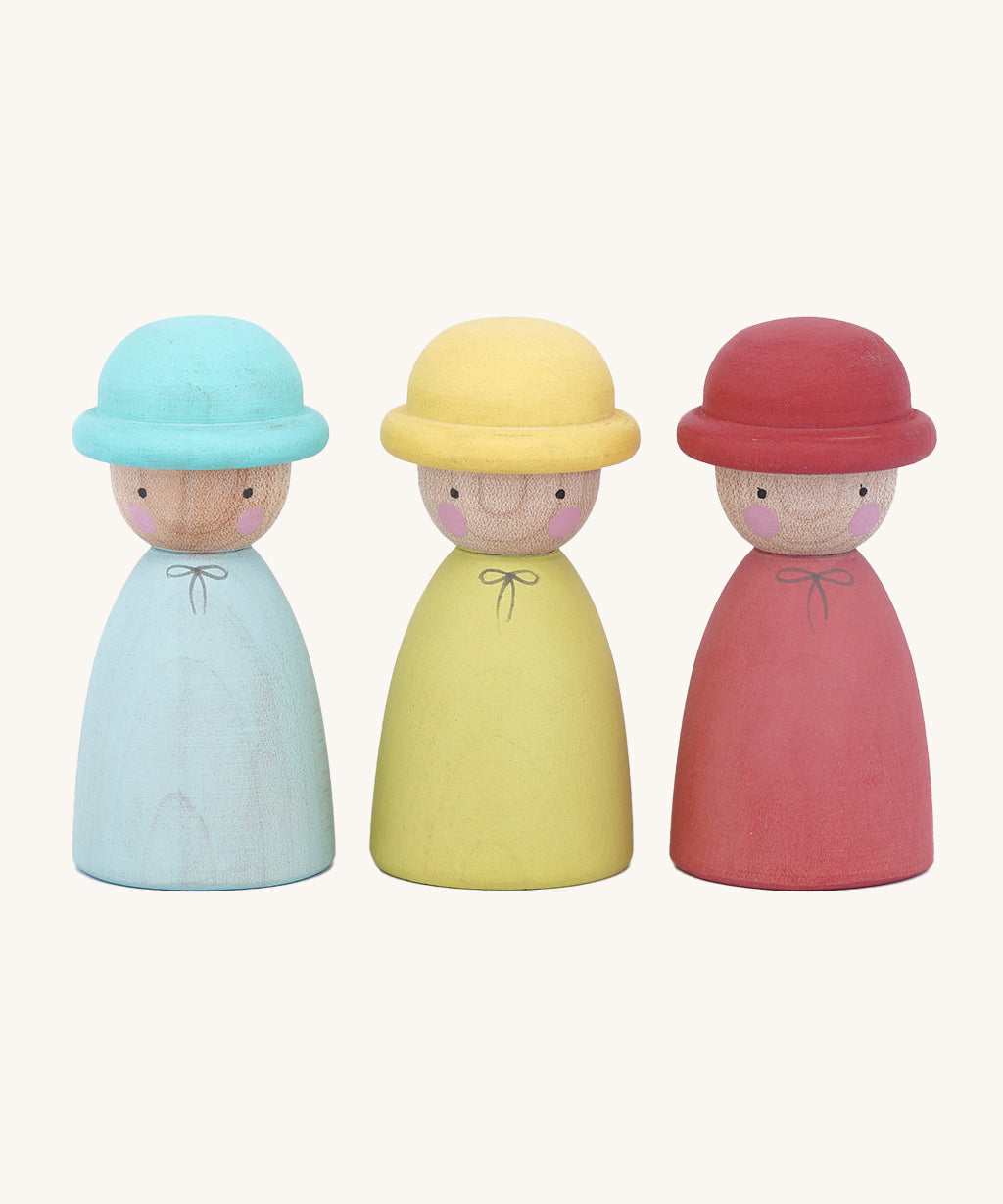 The Peepul Three Hatters are Waldorf inspired, wooden peg dolls with little bowler hats. The peg doll on the left is blue with a blue hat, the middle is yellow with a yellow hat, and the one on the right is red with a red hat. Each doll has two small, black eyes and two pink rosy cheeks. The image is on a cream background