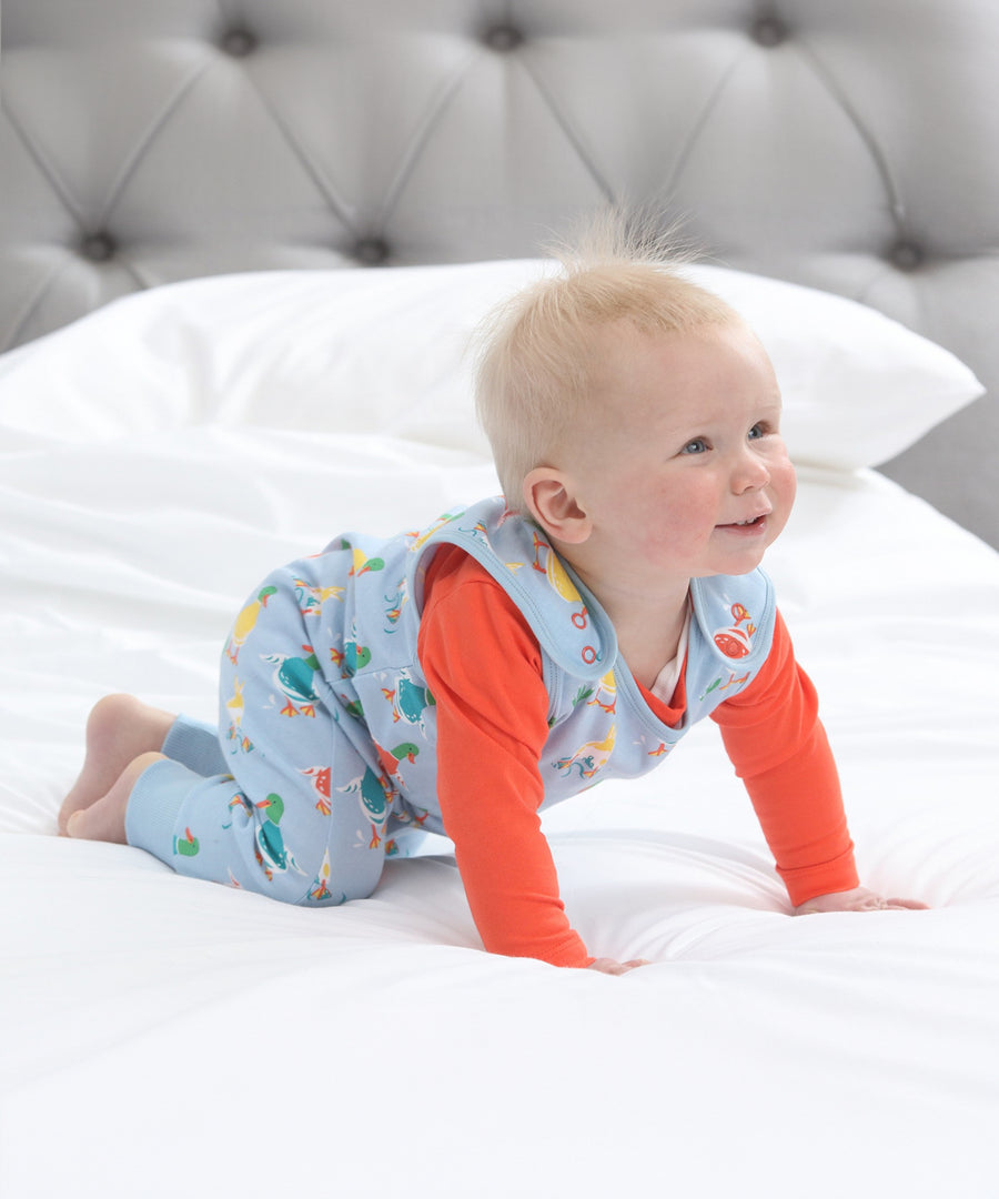 A child crawling, wearing the Piccalilly Duck Days Dungarees. The image shows the popper fasteners on the shoulders