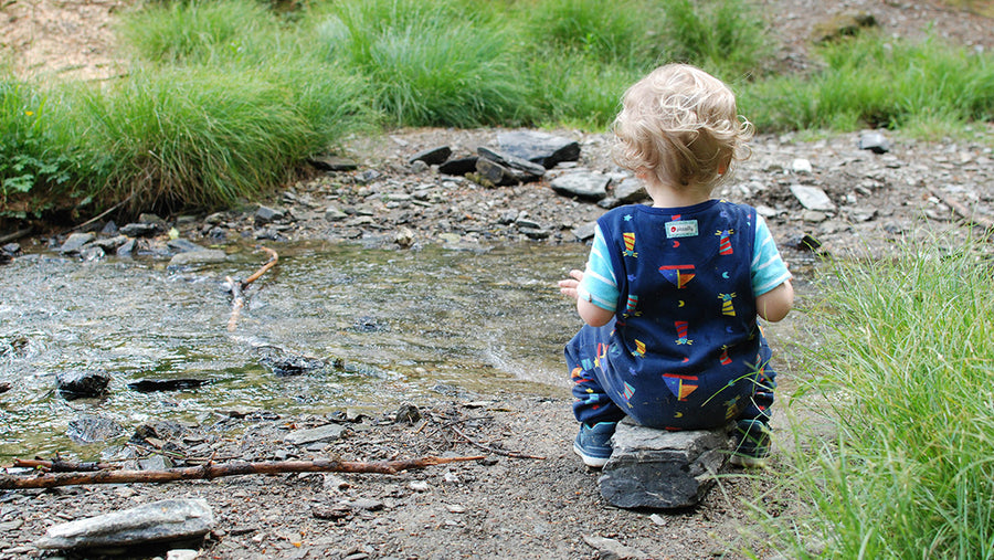 Little child sitting on a riverbank, wearing an organic cotton Piccalilly outfit