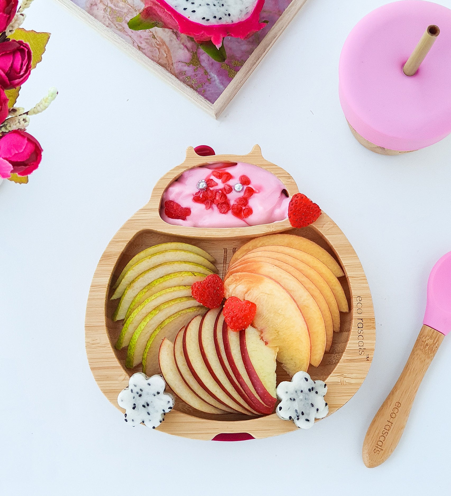 Eco Rascals Ladybird Bamboo Suction Plate filled with apple slices, pink yoghurt and decorated with fresh fruit, with a pink bamboo and silicone baby spoon and cup with a straw.