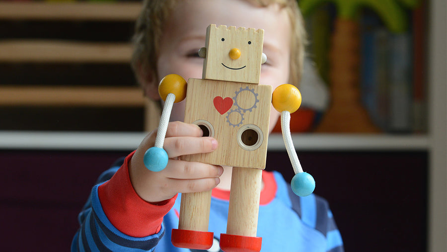 Little boy holding up a Plan Toys wooden robot