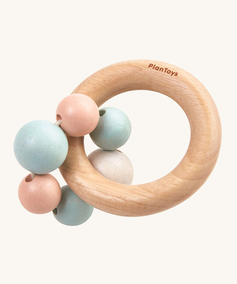 PlanToys Pastel Beads Rattle is a beautifully crafted, wooden baby rattle that is perfect for teething and sore gums. The rattle comes with a wooden ring, and attached to the ring a pastel pink, blue and white beads. The image is on a cream background