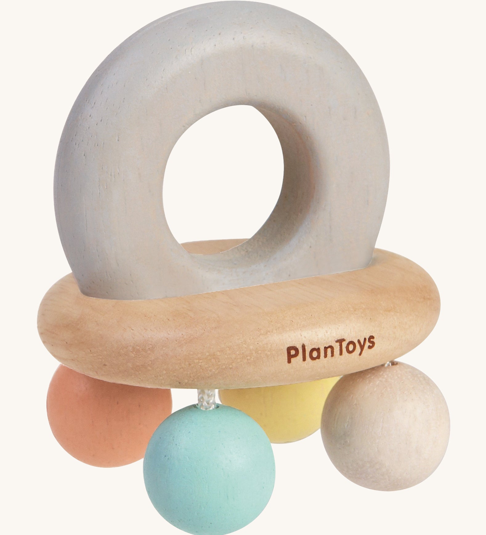 PlanToys Pastel Bell Rattle, is a beautiful wooden baby toy. The rattle comes in the shape of a bell, with a large soft grey wooden ring on top for easy gripping. At the bottom of the ring is a horizontal wooden oval, and attached to the wooden oval are four pastel coloured balls in blue, white, peach and yellow. The image is on a cream background