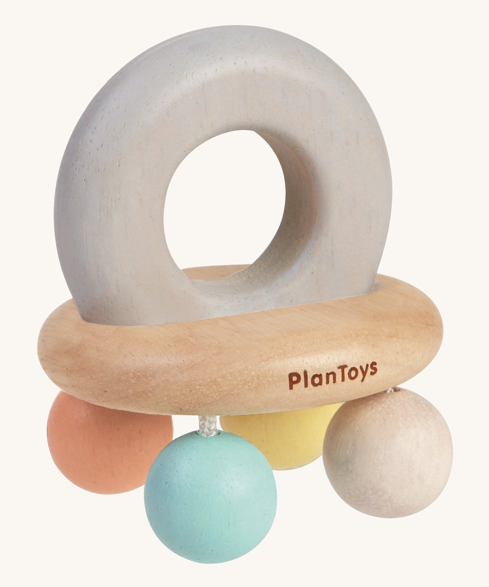 PlanToys Pastel Bell Rattle, is a beautiful wooden baby toy. The rattle comes in the shape of a bell, with a large soft grey wooden ring on top for easy gripping. At the bottom of the ring is a horizontal wooden oval, and attached to the wooden oval are four pastel coloured balls in blue, white, peach and yellow. The image is on a cream background