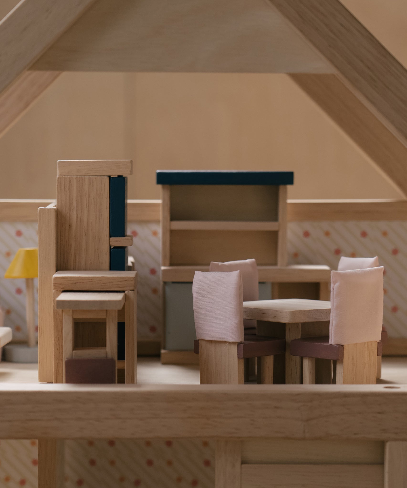 A side on view of the pieces from the PlanToys Dining Room Dolls House Furniture set set up in a wooden dolls house. 