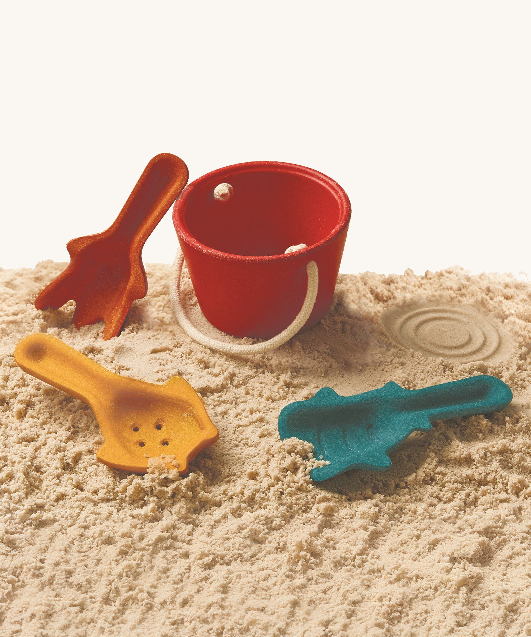 The PlanToys Sand Play Set laid out on soft sand and on a cream background