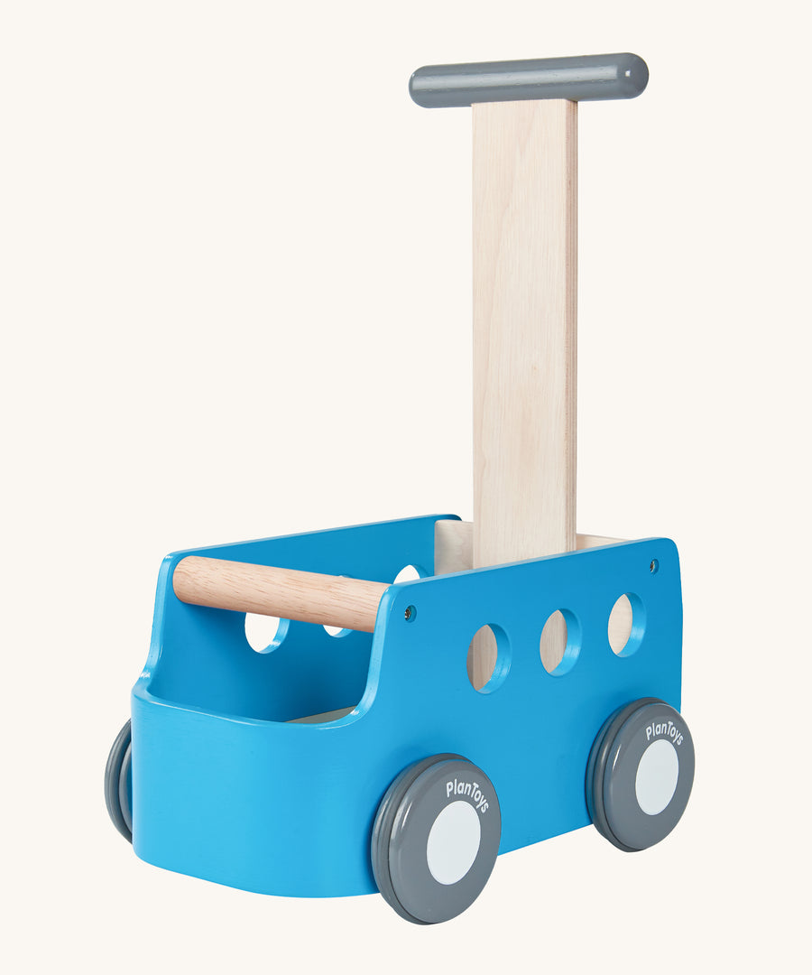 The PlanToys Blue Van Walker is a 2 in 1 toy as a walker and a storage toy box. The van is blue with grey wheels which have "PlanToys" painted onto them, a grey handle with a natural wood section connecting the handle to the van. The image is on a cream background