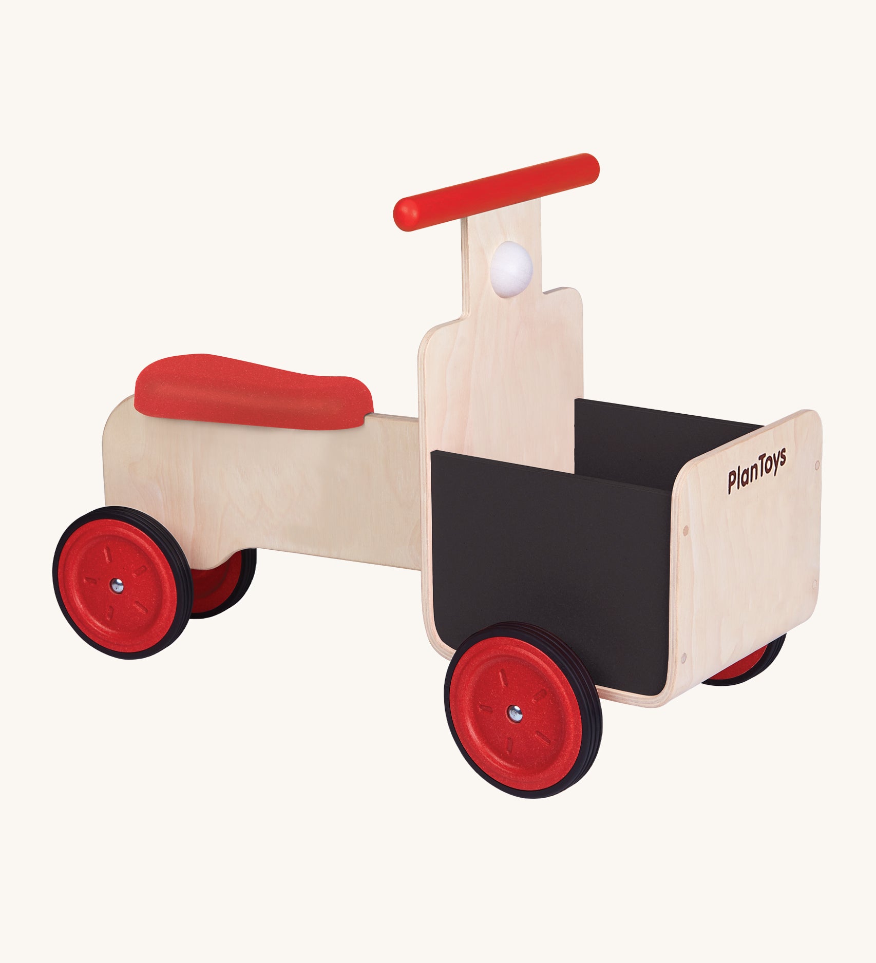 The PlanToys Delivery Bike, is a fun, wooden ride on bike which can be used in a push and pull motion by the child's feet. The bike has 4 red wheels, a red seat, a red handle, a black basket on the front, and a white horn underneath the handle. The image is on a cream background.