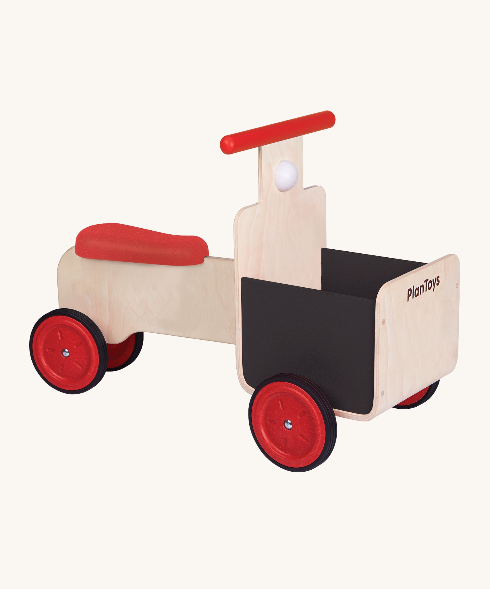 The PlanToys Delivery Bike, is a fun, wooden ride on bike which can be used in a push and pull motion by the child's feet. The bike has 4 red wheels, a red seat, a red handle, a black basket on the front, and a white horn underneath the handle. The image is on a cream background.