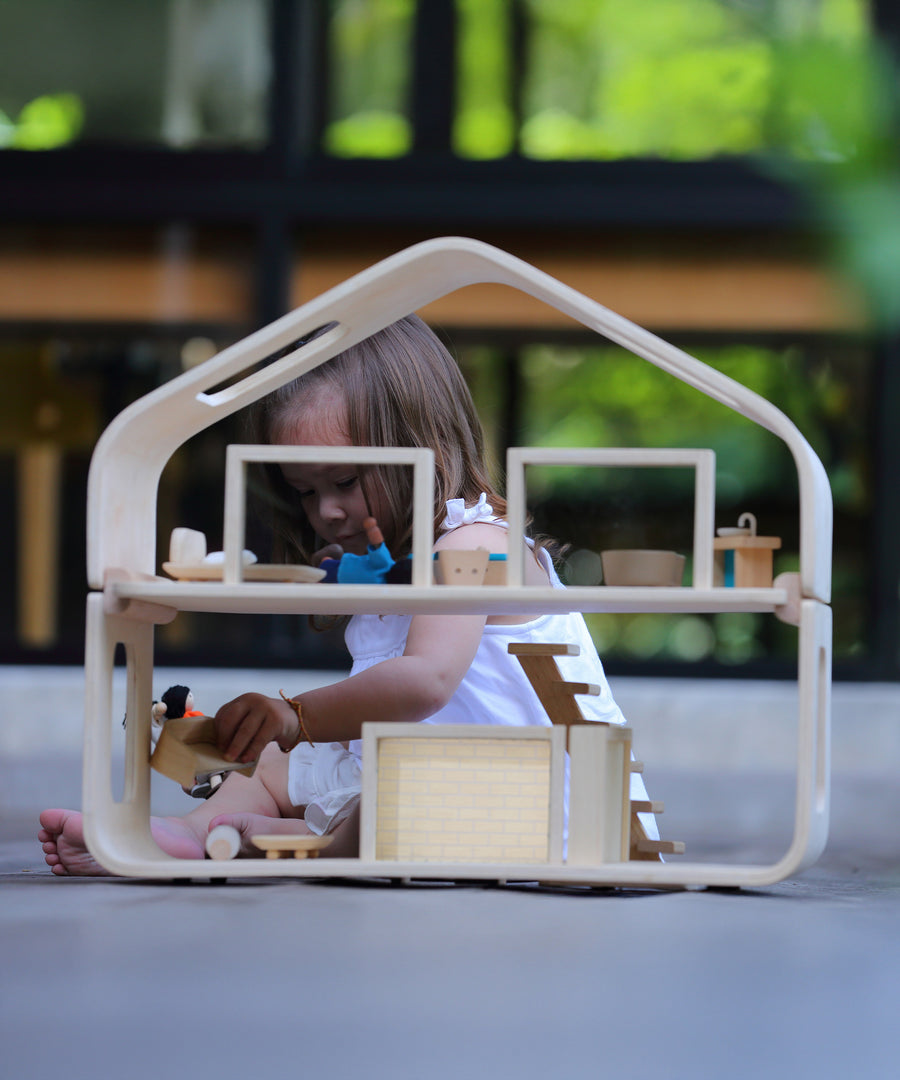 A child playing with the PlanToys Contemporary Dolls House. There are wooden dolls and wooden furniture inside. 