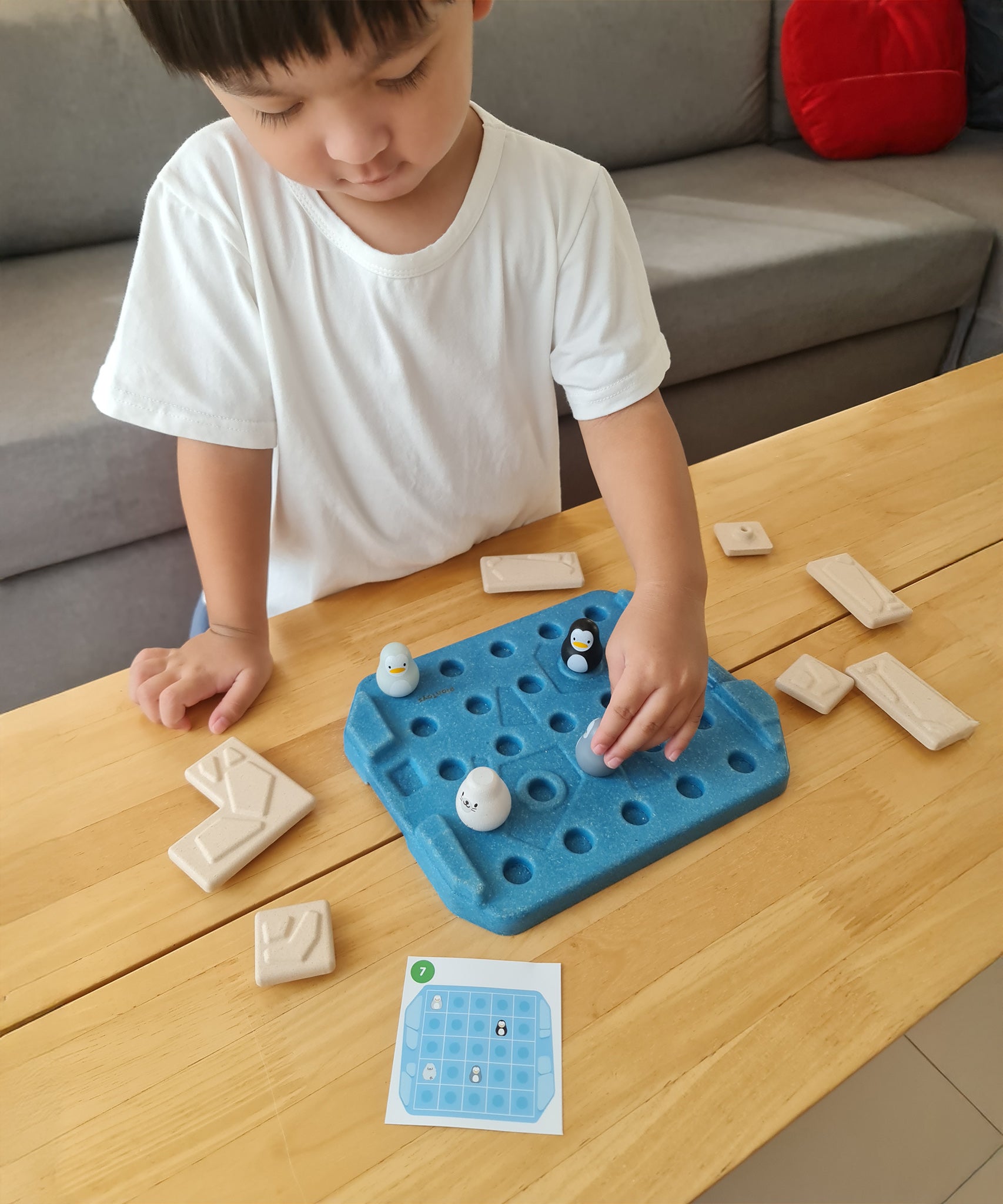 Close up of a child picking up a penguin piece from the Plan Toys eco-friendly wooden finding penguin game on a wooden table