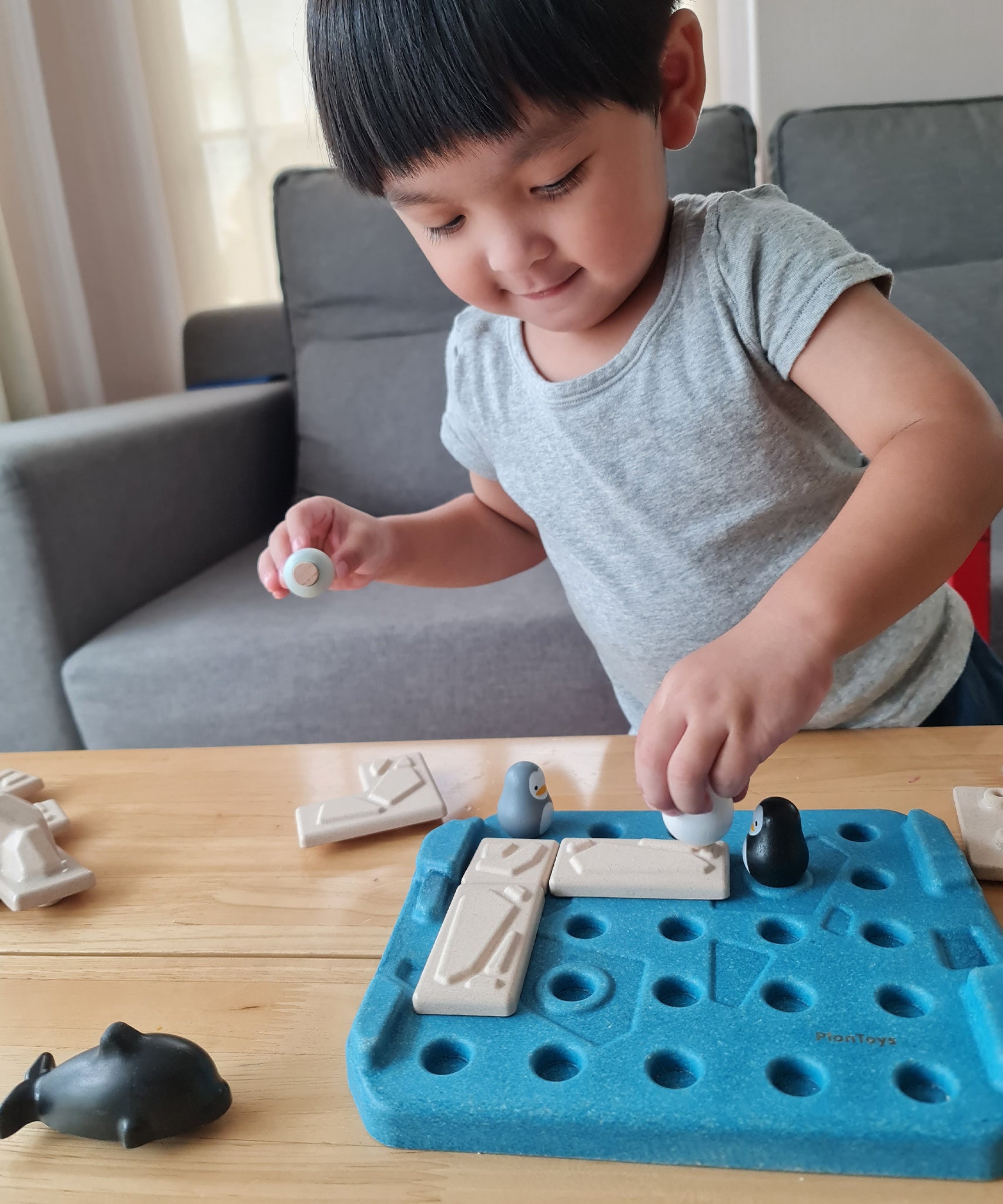 Boy moving the pieces of the Plan Toys plastic free finding penguin family board game on a light wooden table