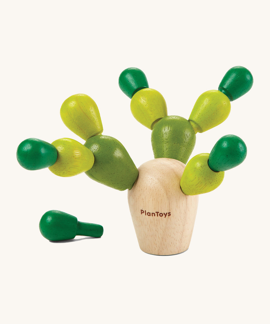 The PlanToys Mini Balancing Cactus with a natural wooden block where the green coloured pegs go into, to create a cactus shaped toy. The image is on a cream background