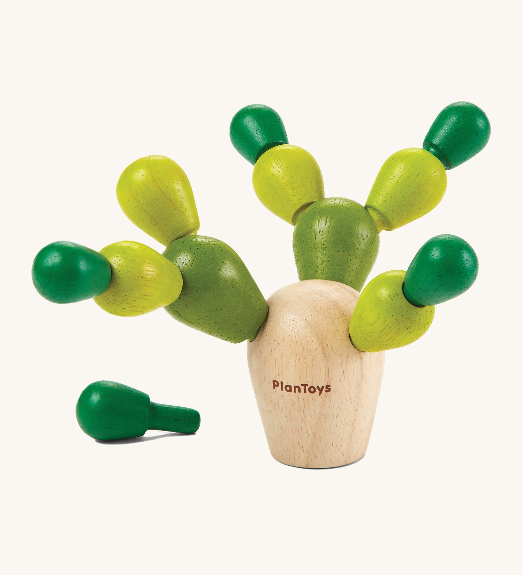 The PlanToys Mini Balancing Cactus with a natural wooden block where the green coloured pegs go into, to create a cactus shaped toy. The image is on a cream background