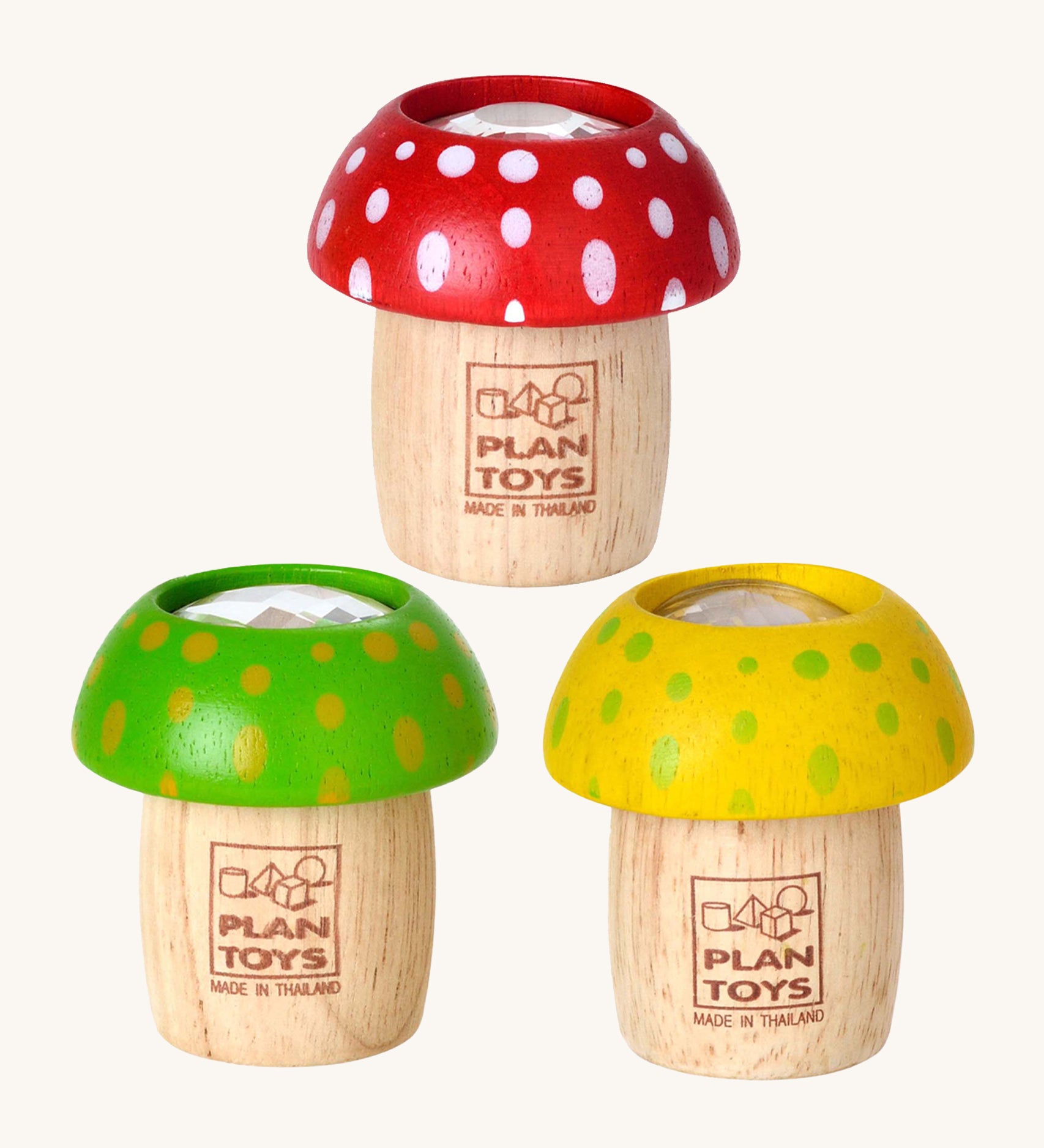 The PlanToys Mushroom Kaleidoscopes look just like a real toy mushroom, and a fun sensory experience. The one at the top is red with white spots, the bottom left is green with yellow spots, and the bottom right is yellow with green spots. The image is on a cream background.