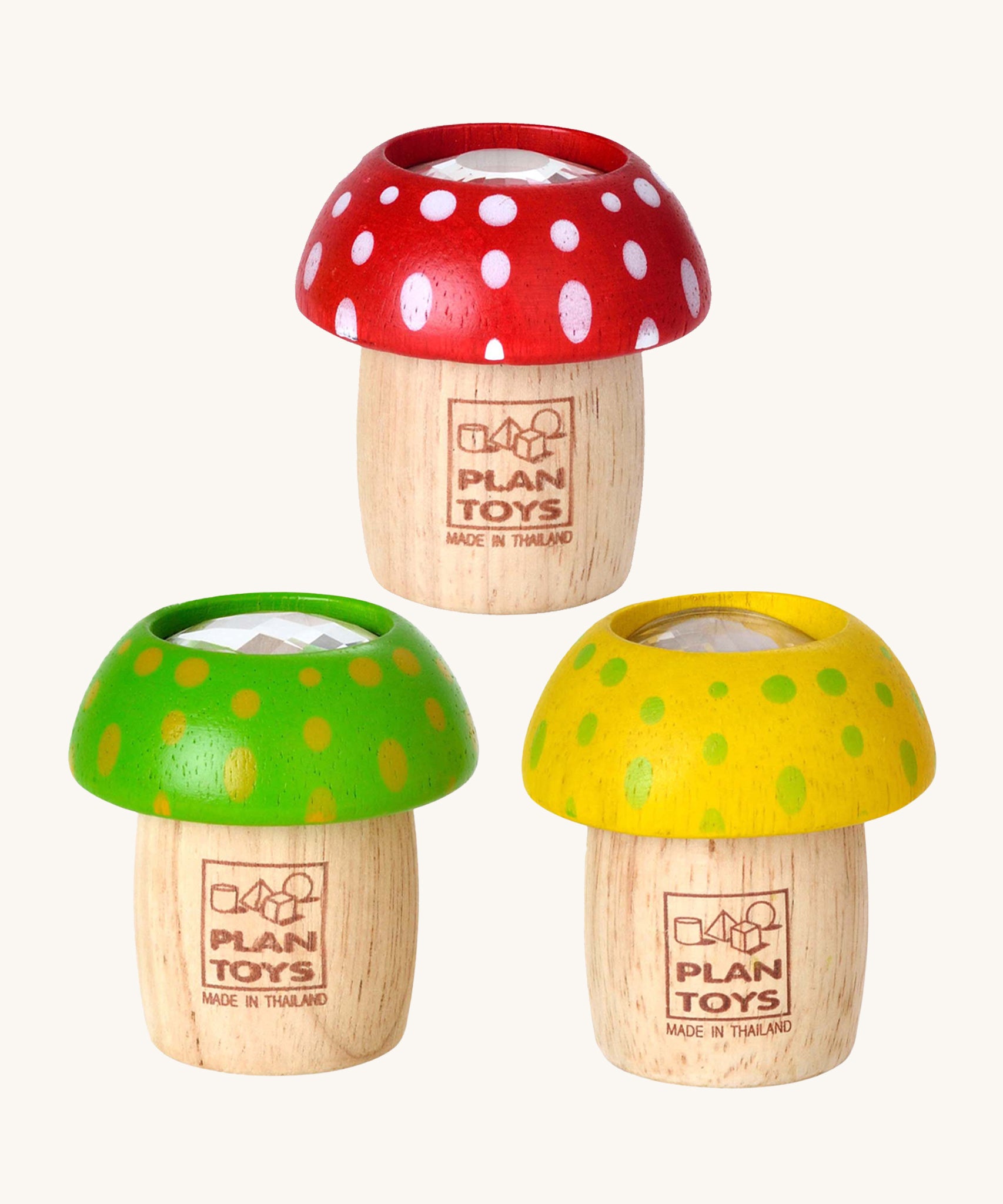 The PlanToys Mushroom Kaleidoscopes look just like a real toy mushroom, and a fun sensory experience. The one at the top is red with white spots, the bottom left is green with yellow spots, and the bottom right is yellow with green spots. The image is on a cream background.