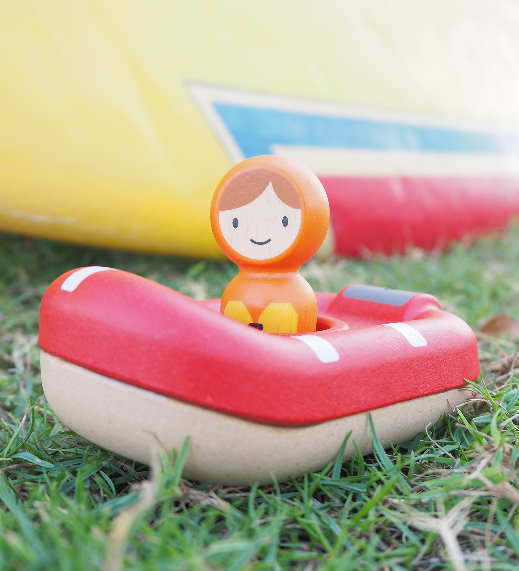 The PlanToys Coast Guard Boat Bath Toy laid on a grassy floor and being played with outside