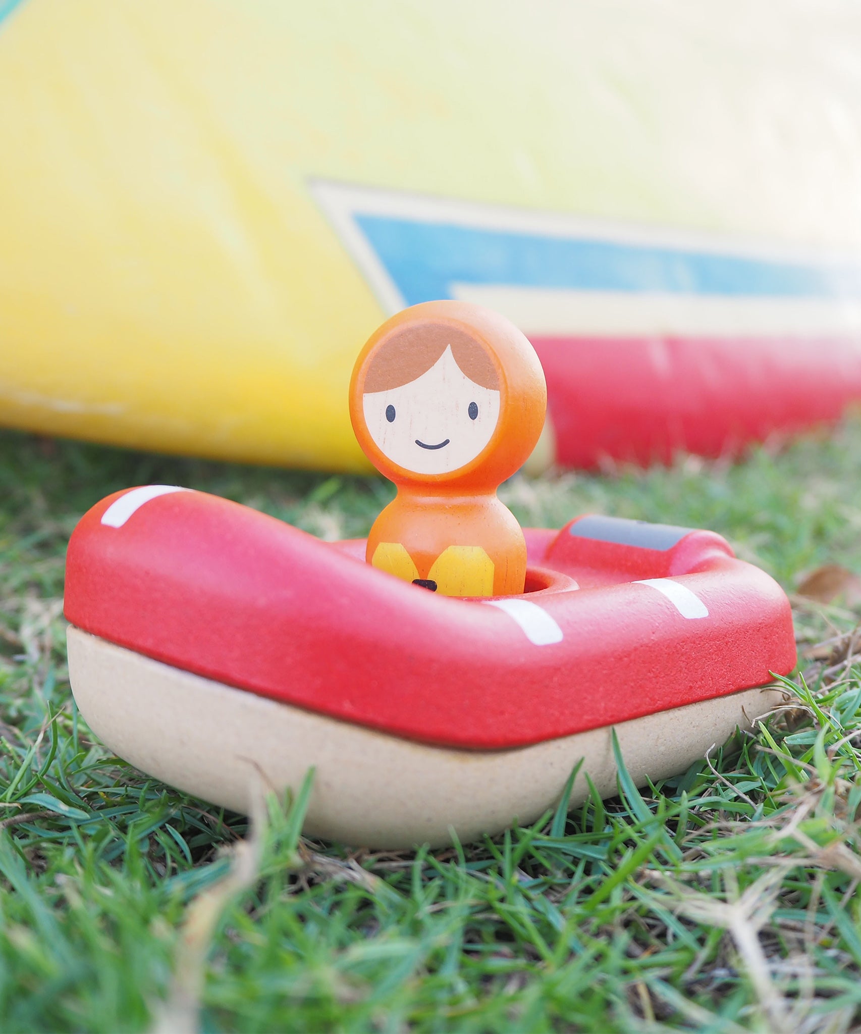 The PlanToys Coast Guard Boat Bath Toy laid on a grassy floor and being played with outside