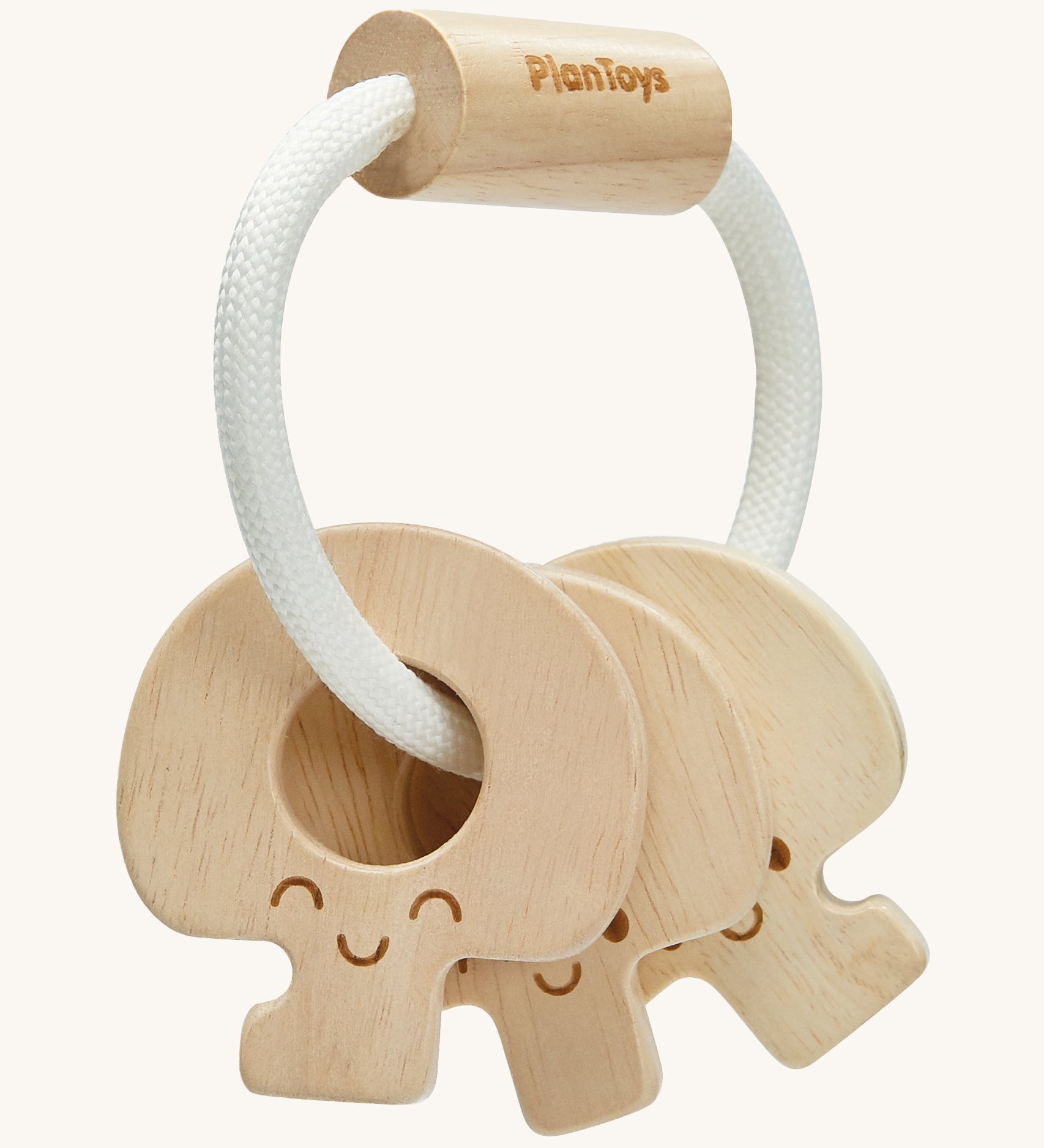 PlanToys Wooden Baby Key Rattle is a fun sensory toy for little ones. This toy is great for teething and soothing sore gums. There is a circular white rope with a wooden bead at the top. Attached to the rope are three, natural wooden keys, all with smiling faces. The image is on a cream background.