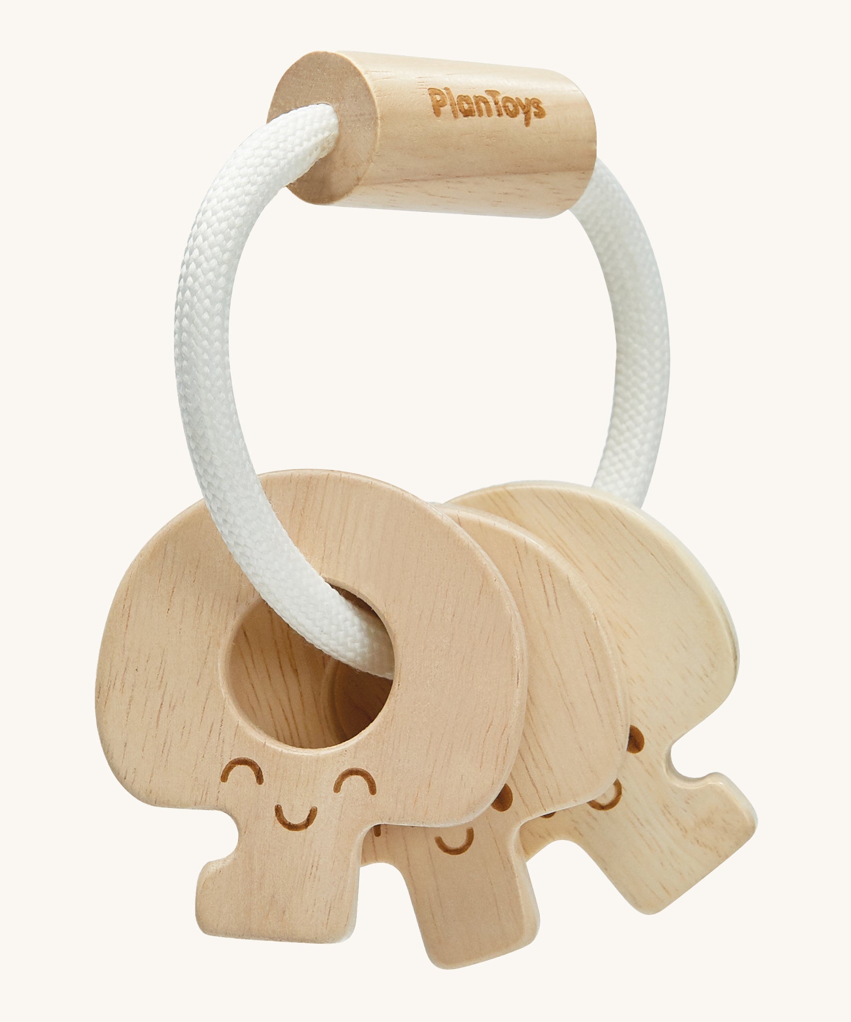 PlanToys Wooden Baby Key Rattle is a fun sensory toy for little ones. This toy is great for teething and soothing sore gums. There is a circular white rope with a wooden bead at the top. Attached to the rope are three, natural wooden keys, all with smiling faces. The image is on a cream background.