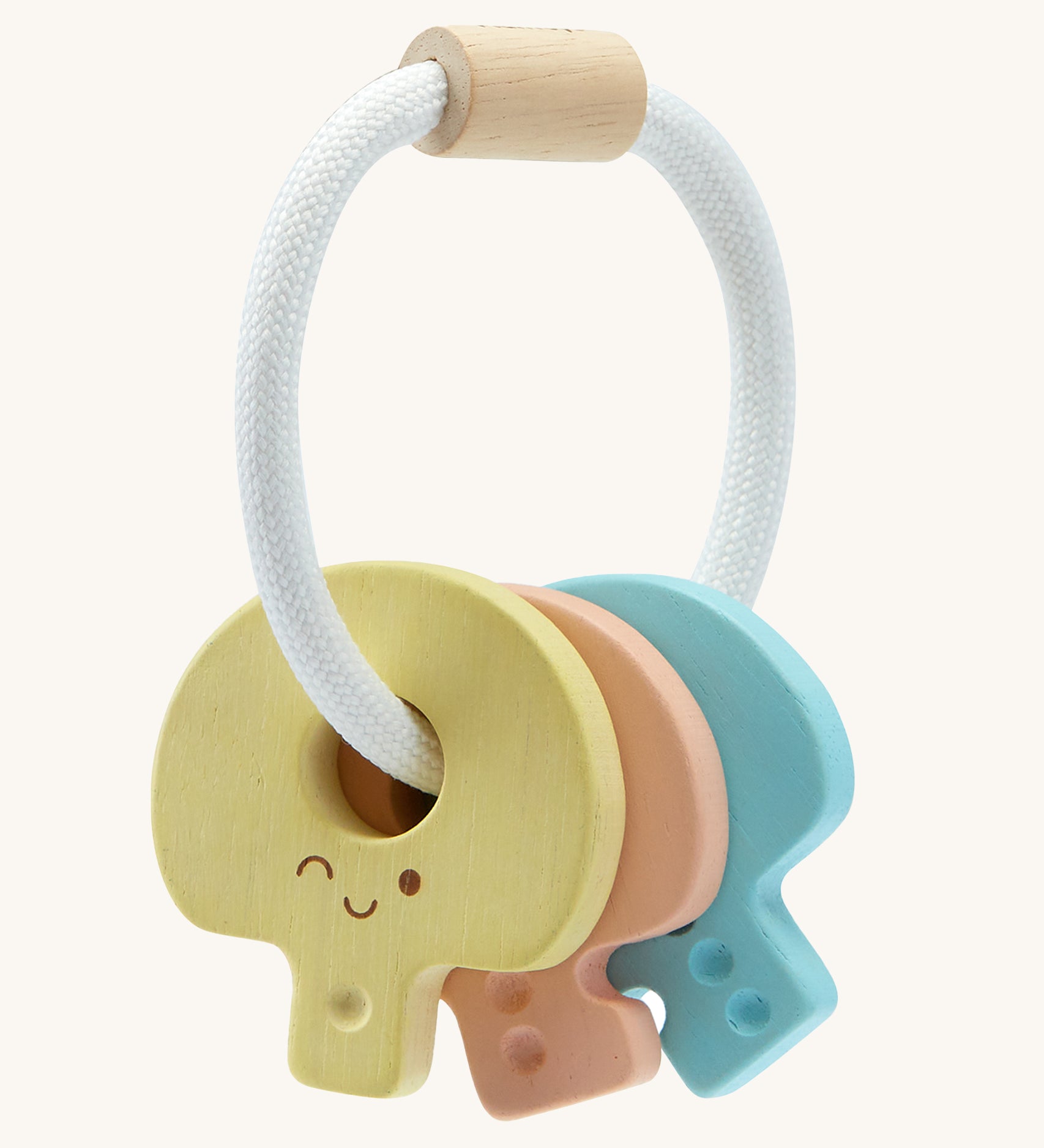 PlanToys Wooden Baby Key Rattle is a fun sensory toy for little ones. This toy is great for teething and soothing sore gums. There is a circular white rope with a wooden bead at the top. Attached to the rope are three, colourful pastel wooden keys, all with smiling faces and dots to correspond to the key. The yellow key has one dot, the peach key has two dots, and the blue key has three dots. The image is on a cream background.