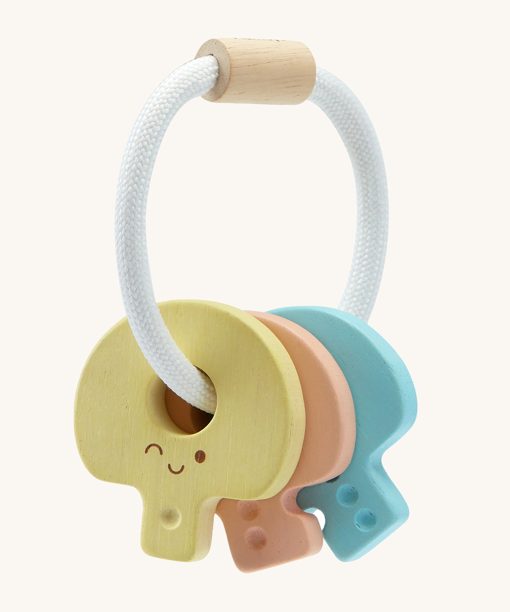 PlanToys Wooden Baby Key Rattle is a fun sensory toy for little ones. This toy is great for teething and soothing sore gums. There is a circular white rope with a wooden bead at the top. Attached to the rope are three, colourful pastel wooden keys, all with smiling faces and dots to correspond to the key. The yellow key has one dot, the peach key has two dots, and the blue key has three dots. The image is on a cream background.