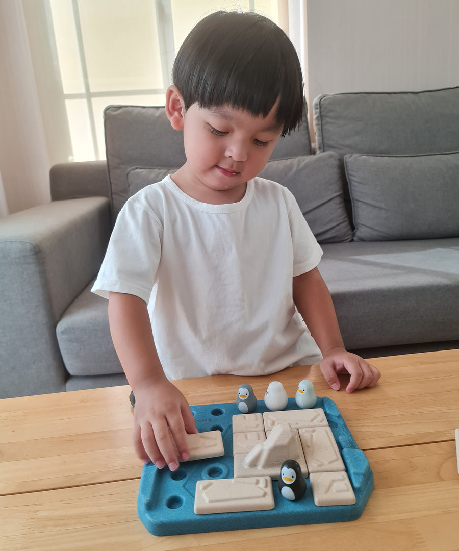 Close up of a child picking up a rectangle piece from the Plan Toys eco-friendly wooden finding penguin game on a wooden table