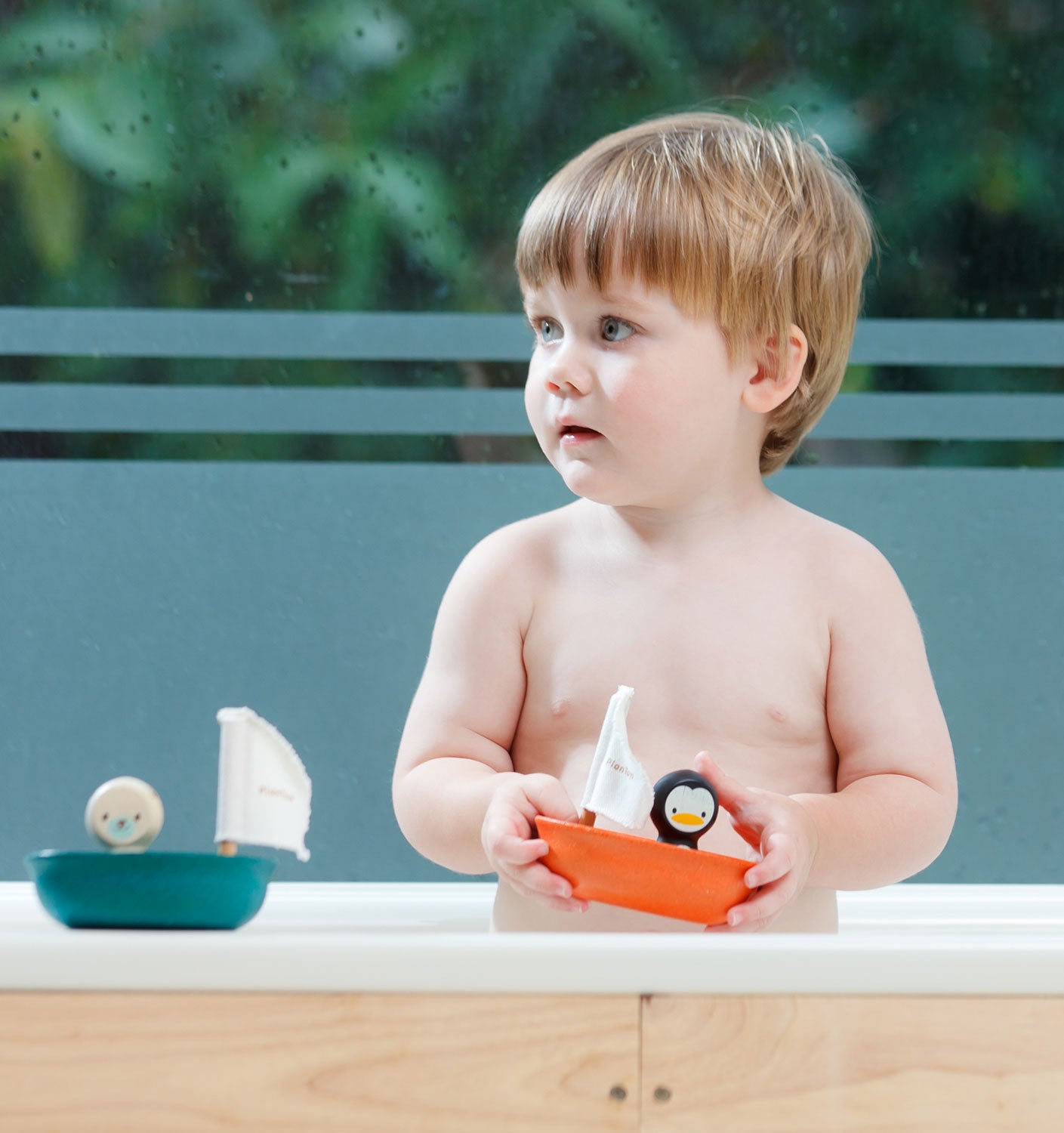 A child playing with a Plan Toys penguin Sailing Boat, there is a Plan Toys Polar Bear Sailing Boat next to him too. 