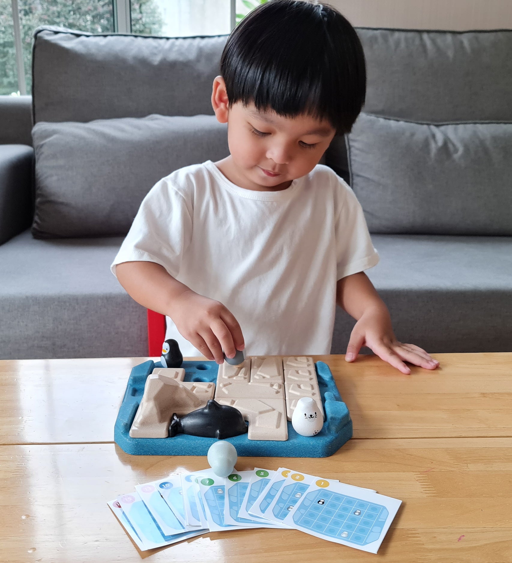 Child playing with the Plan Toys eco-friendly penguin themed family game on a wooden table