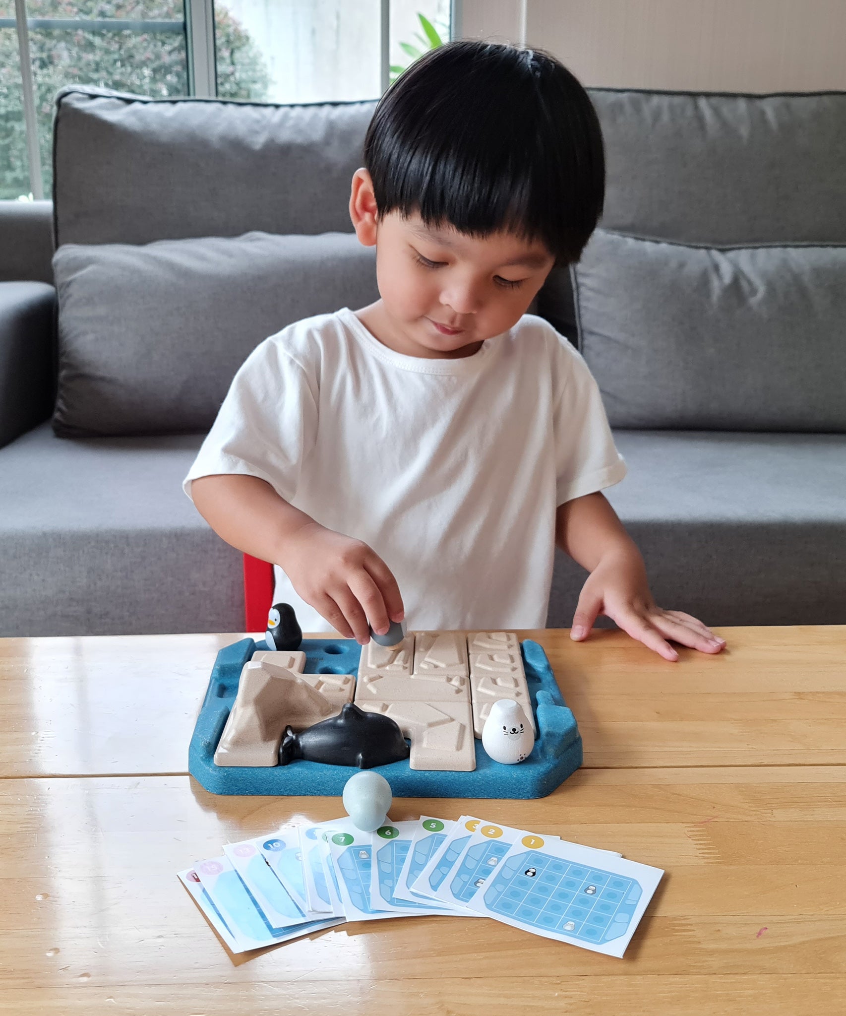 Child playing with the Plan Toys eco-friendly penguin themed family game on a wooden table