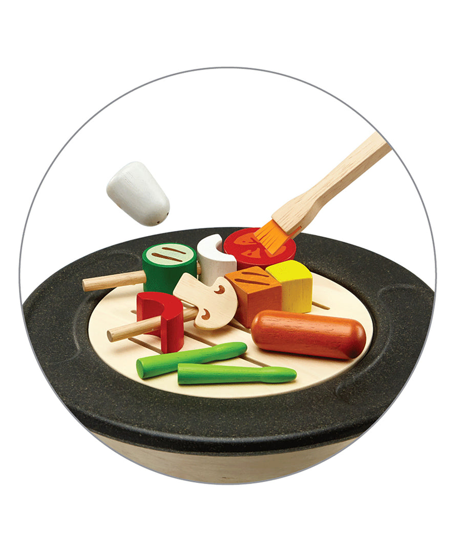 A closer view of the PlanToys BBQ play food which includes wooden bbq food on skewers, the salt shaker and the basting brush