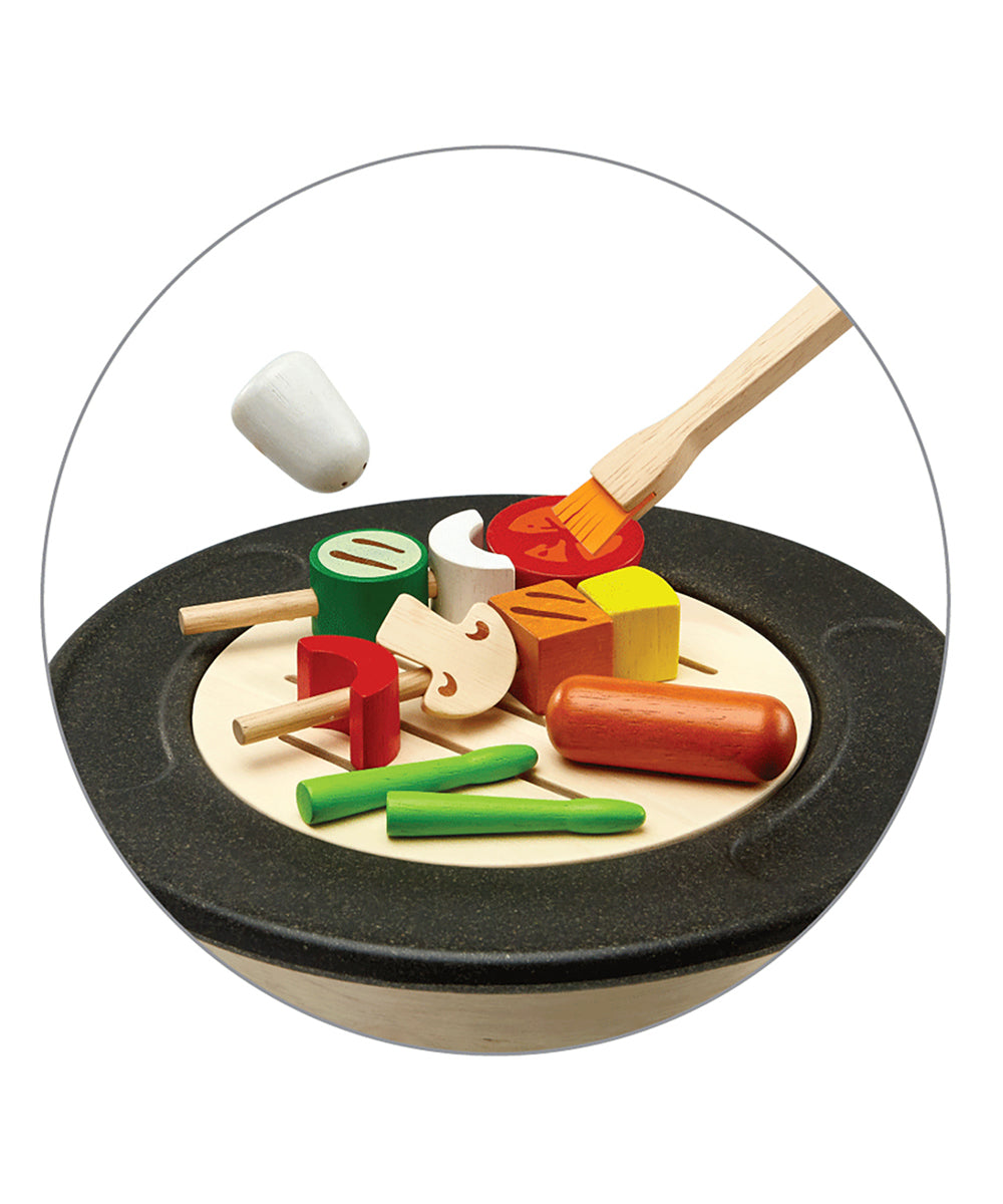 A closer view of the PlanToys BBQ play food which includes wooden bbq food on skewers, the salt shaker and the basting brush