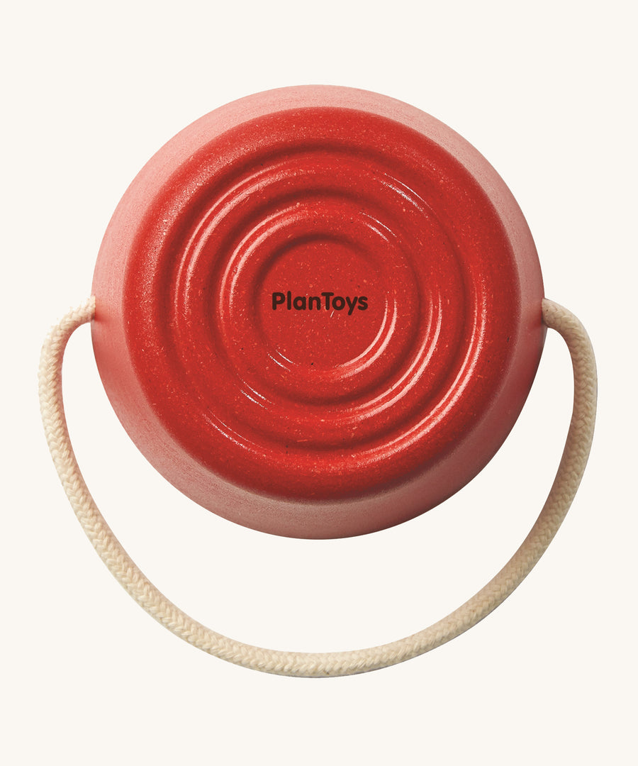 The base of the Plan Toys red bucket from the Sand Play Set showing the beige rope handle and the circle pattern base on the bottom