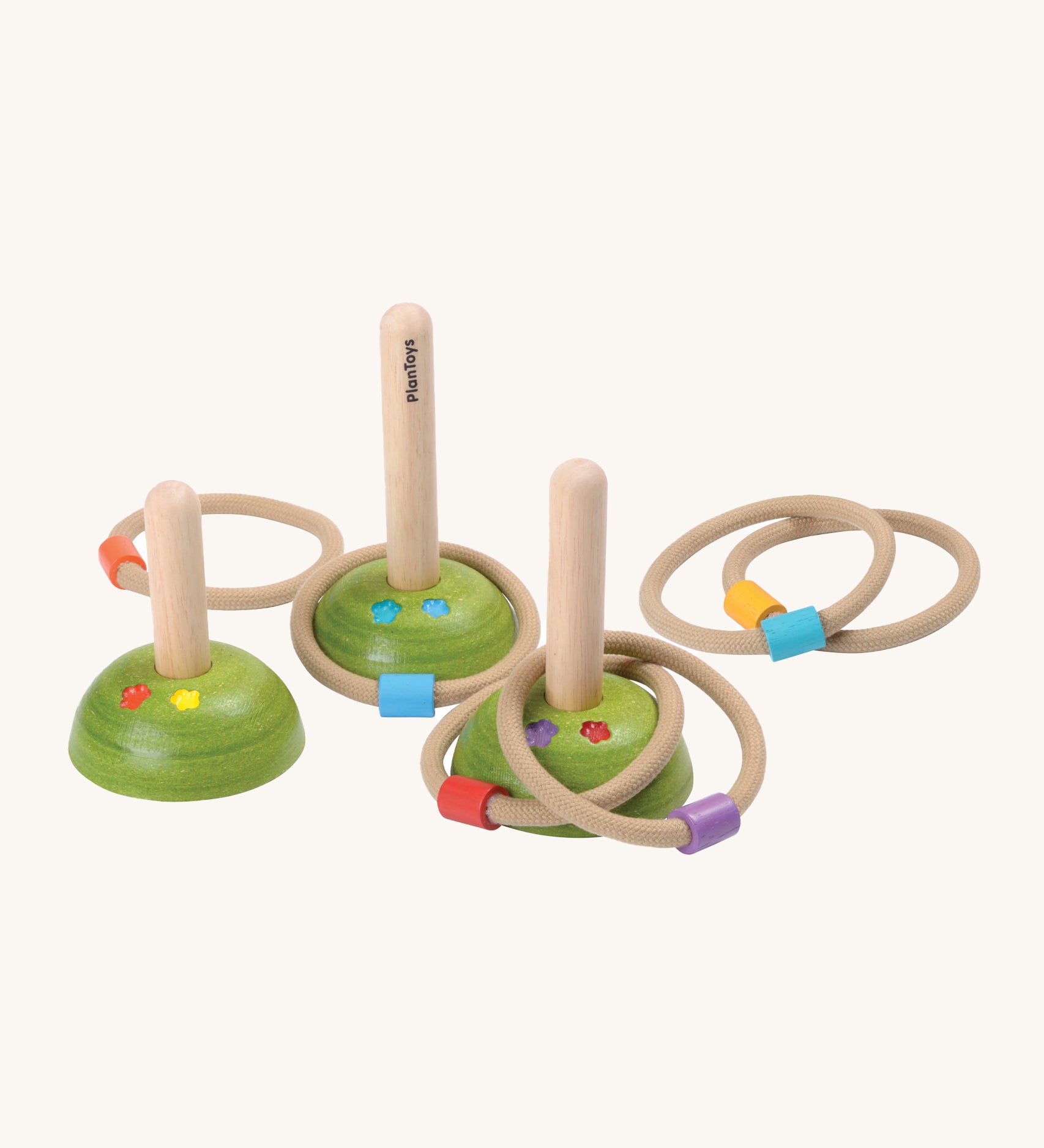 PlanToys Meadow Ring Toss, comes with 3 wooden pegs with green bases with flowers painted on them, and 6 rope rings with a different colour block on each ring. The image is on a cream background