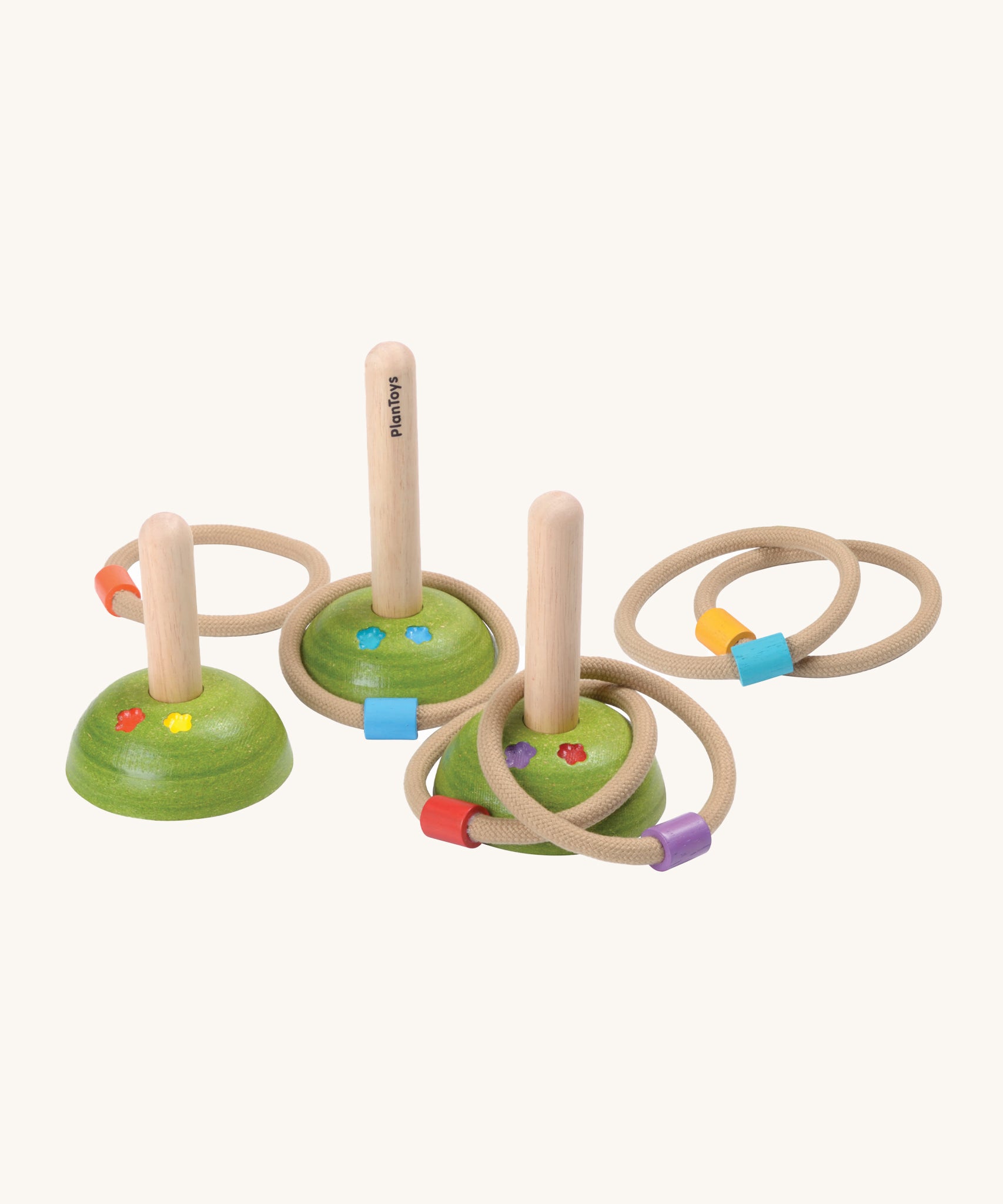 PlanToys Meadow Ring Toss, comes with 3 wooden pegs with green bases with flowers painted on them, and 6 rope rings with a different colour block on each ring. The image is on a cream background